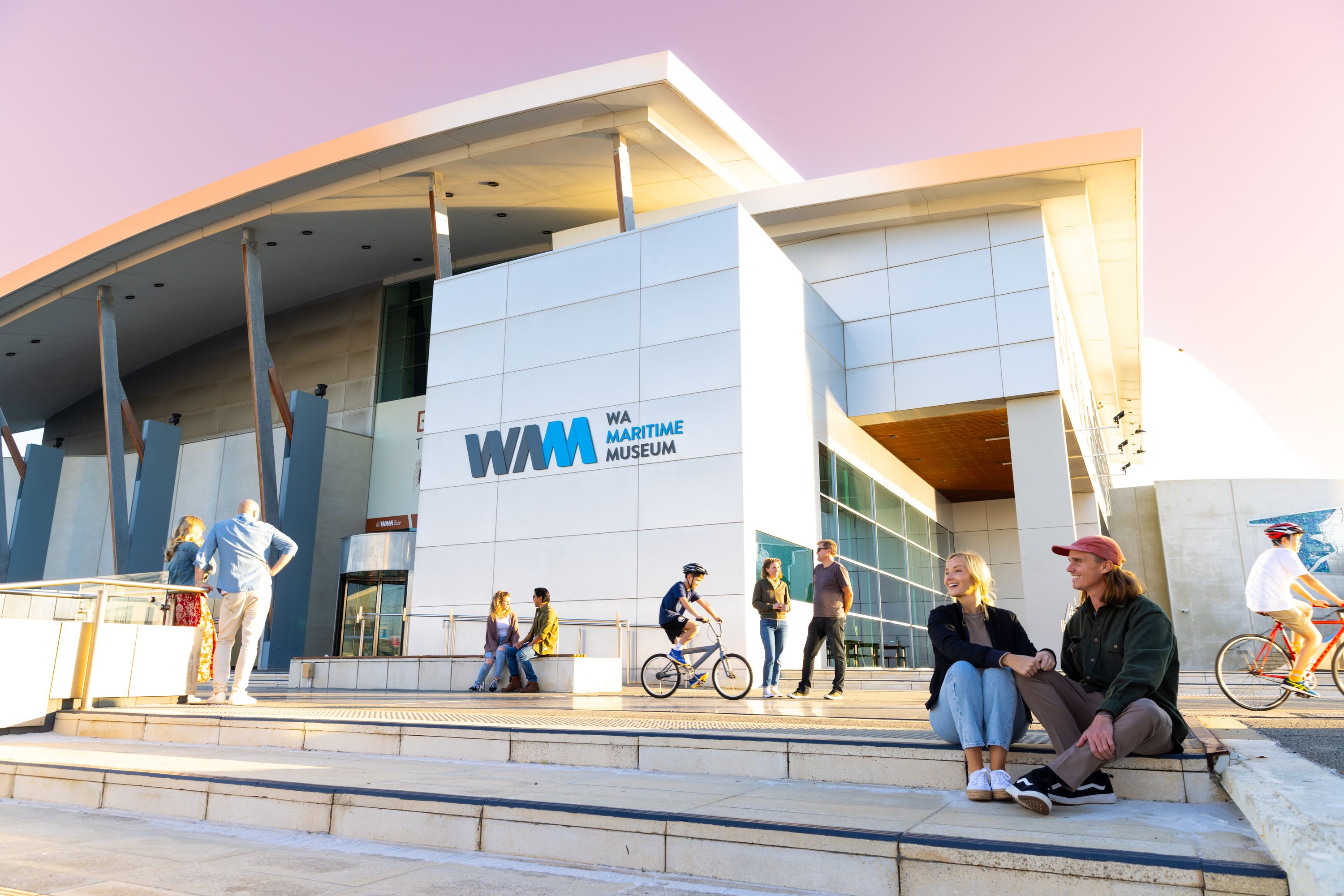 Photo showing the outside of a museum building with people walking and siting around it.