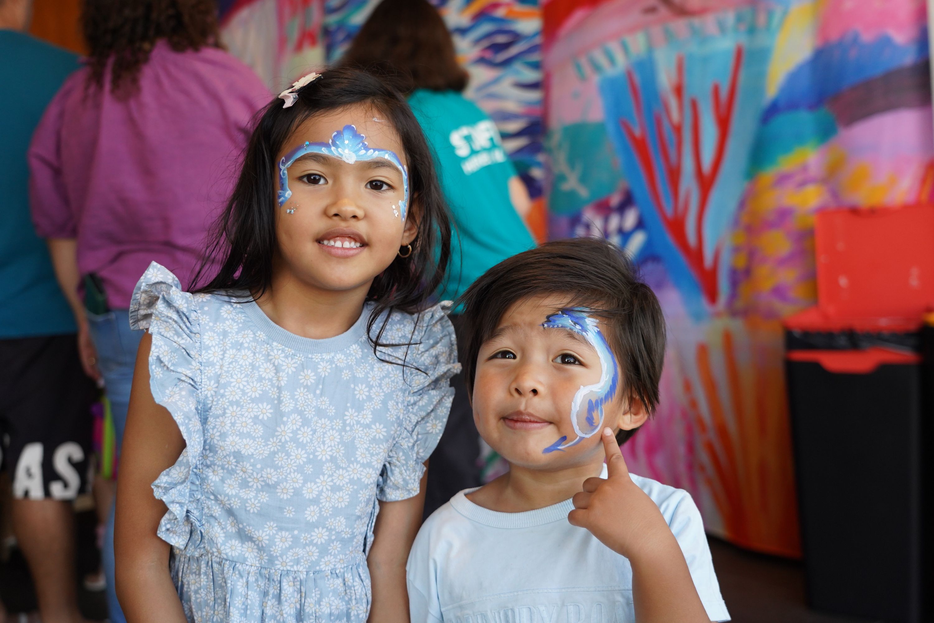 Two children with facepaint. One has a mermaid crown design, the other a blue dragon.