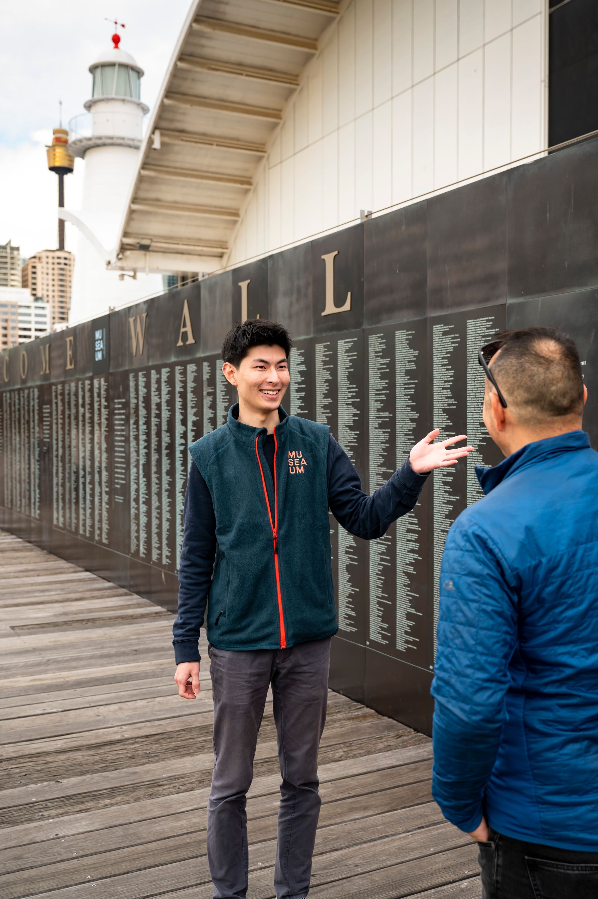 Male volunteer in a uniform showing a visitor names engraved on the national monument to migration
