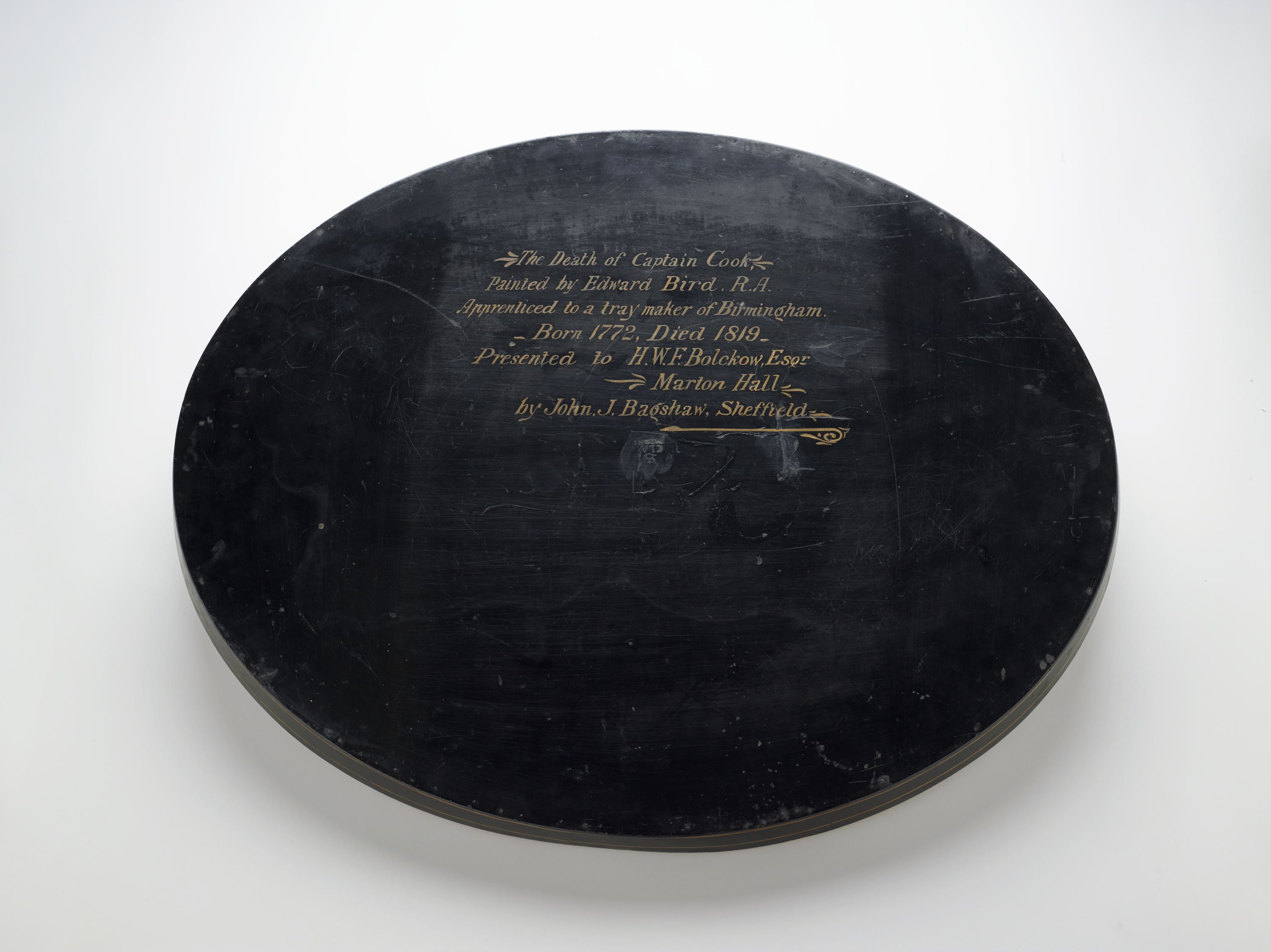 Photo showing the back of a black, wooden tray with gold painted writing. 