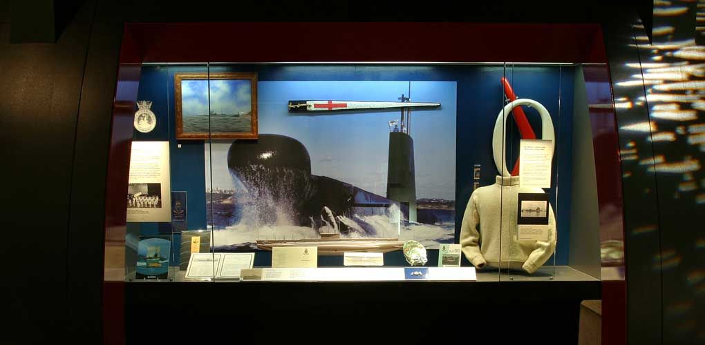 Photo of a museum display case featuring a large photograph of a submarine surrounded by other objects.