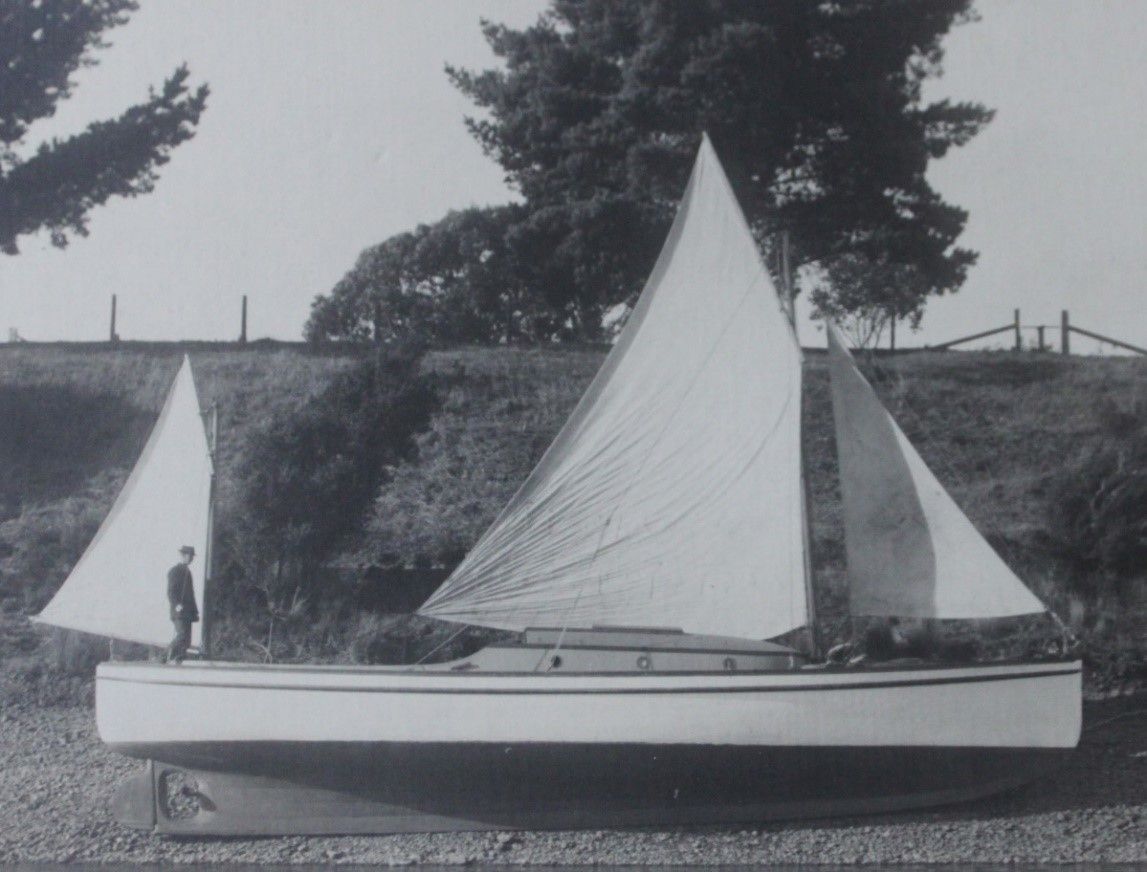 Bkack and white photograph of a boat on the shore, with triangular white sails. There is a man standing on one end.