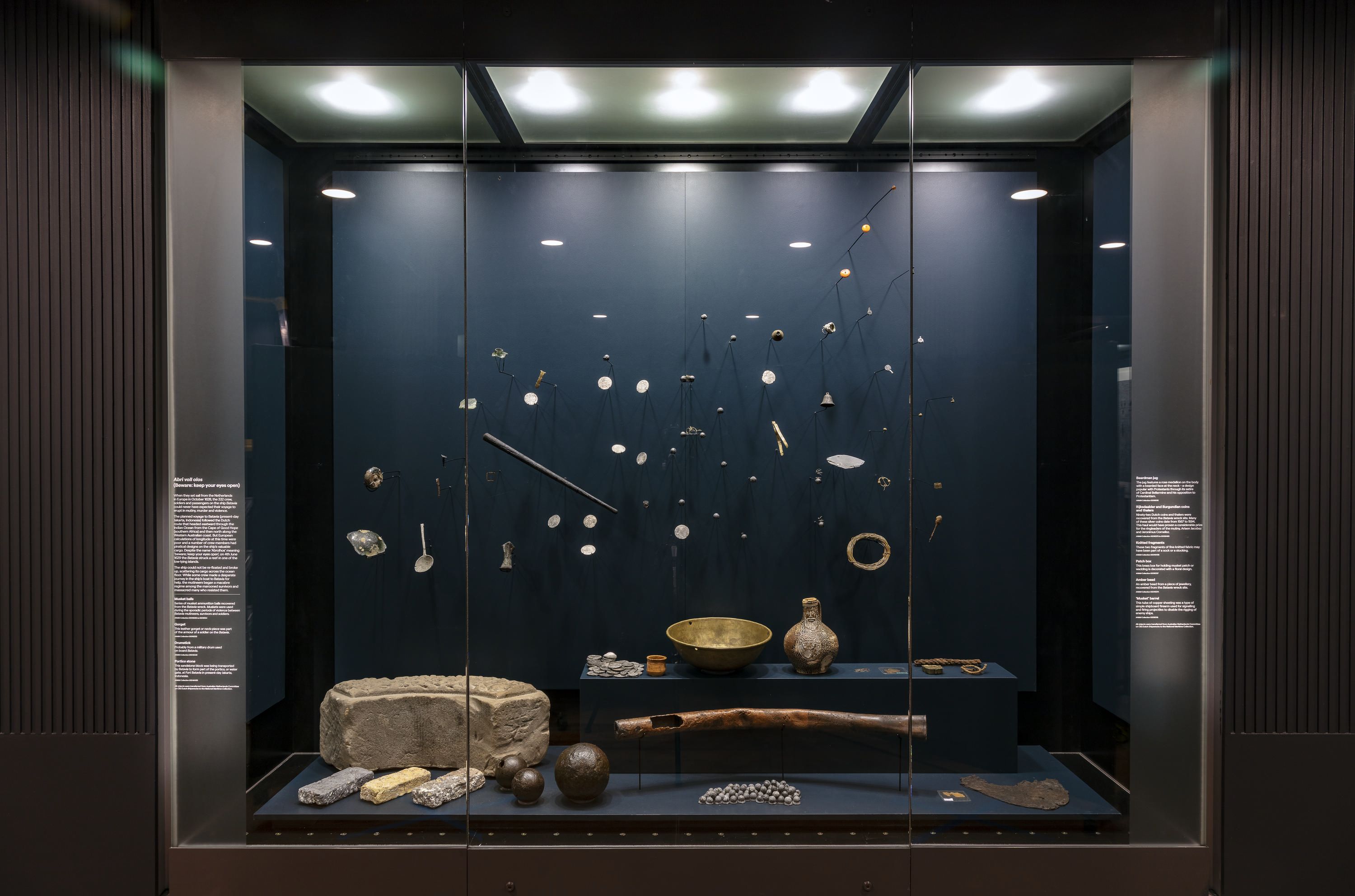 Photo of a museum display case featuring a large number of small objects from a shipwreck. 