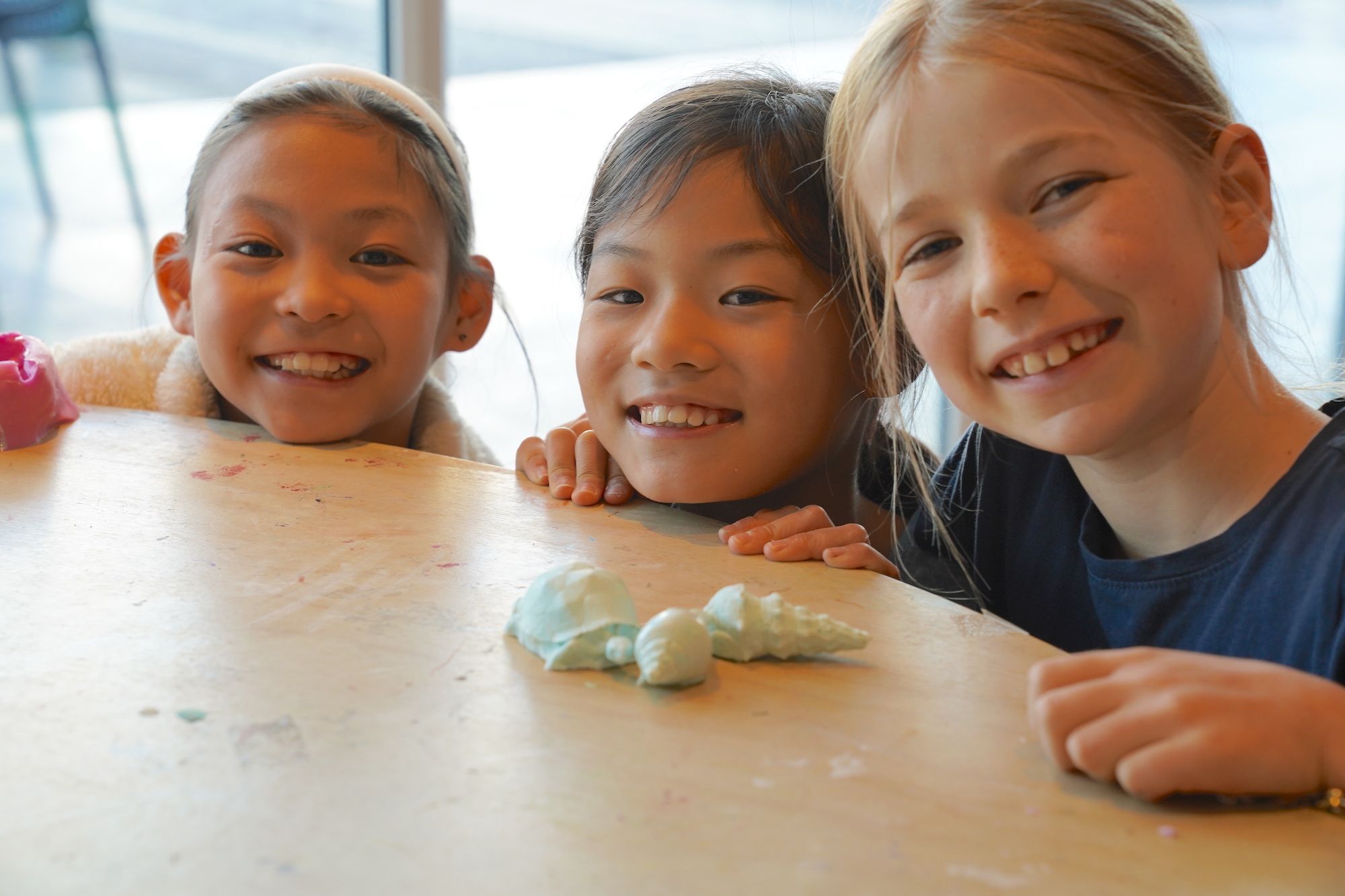 3 girls faces on the edge of a table, with some shell artworks.