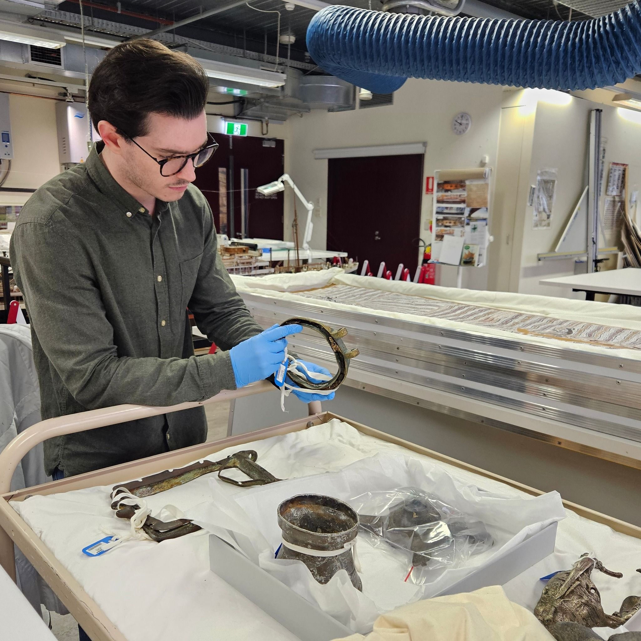 Photo of a man with dark hair and glasses, in a dark shirt and blue gloves holding a round object and standing in a lab.