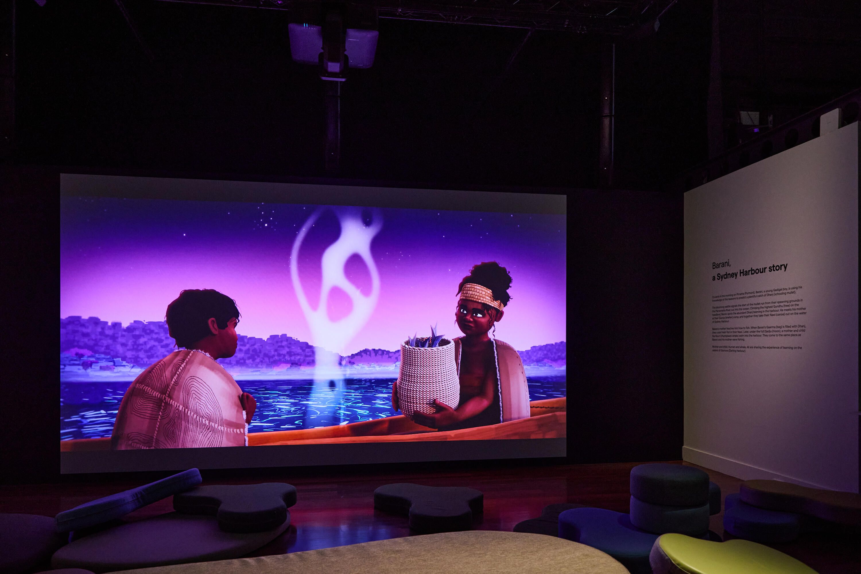 Photo of a museum exhibition space with curved soft seating and a large projection screen