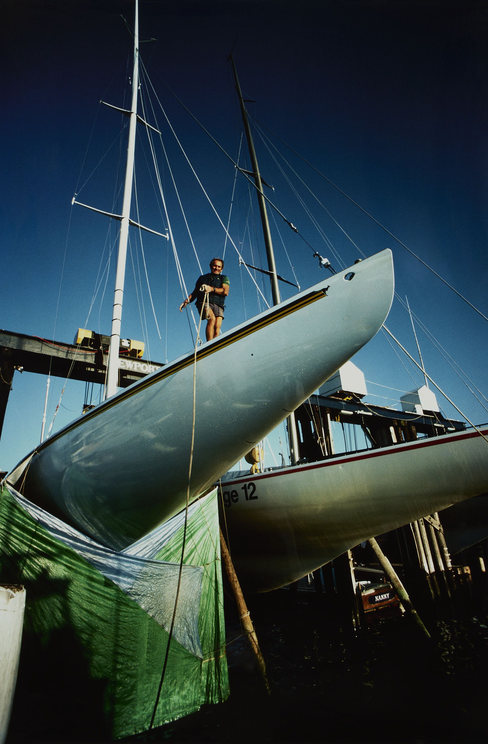 Photo taken from a low angle, of a sailing boat, Australia II with a tarp around it's hull and a man standing on top. 