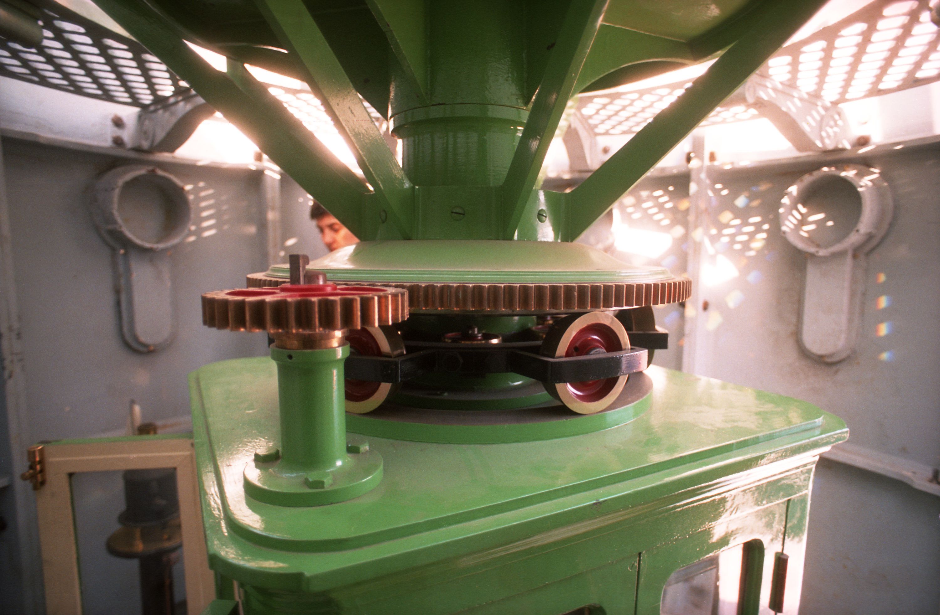 Photo taken inside of the lighthouse showing the lantern pedestal painted green with brass wheels and cogs.