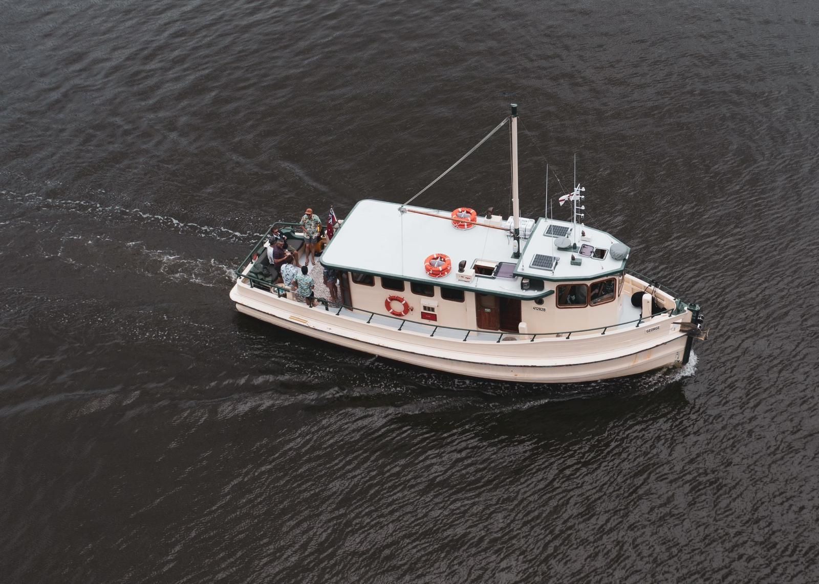 An aerial photograph looking down at a cream and white boat motoring to the right of the frame. 