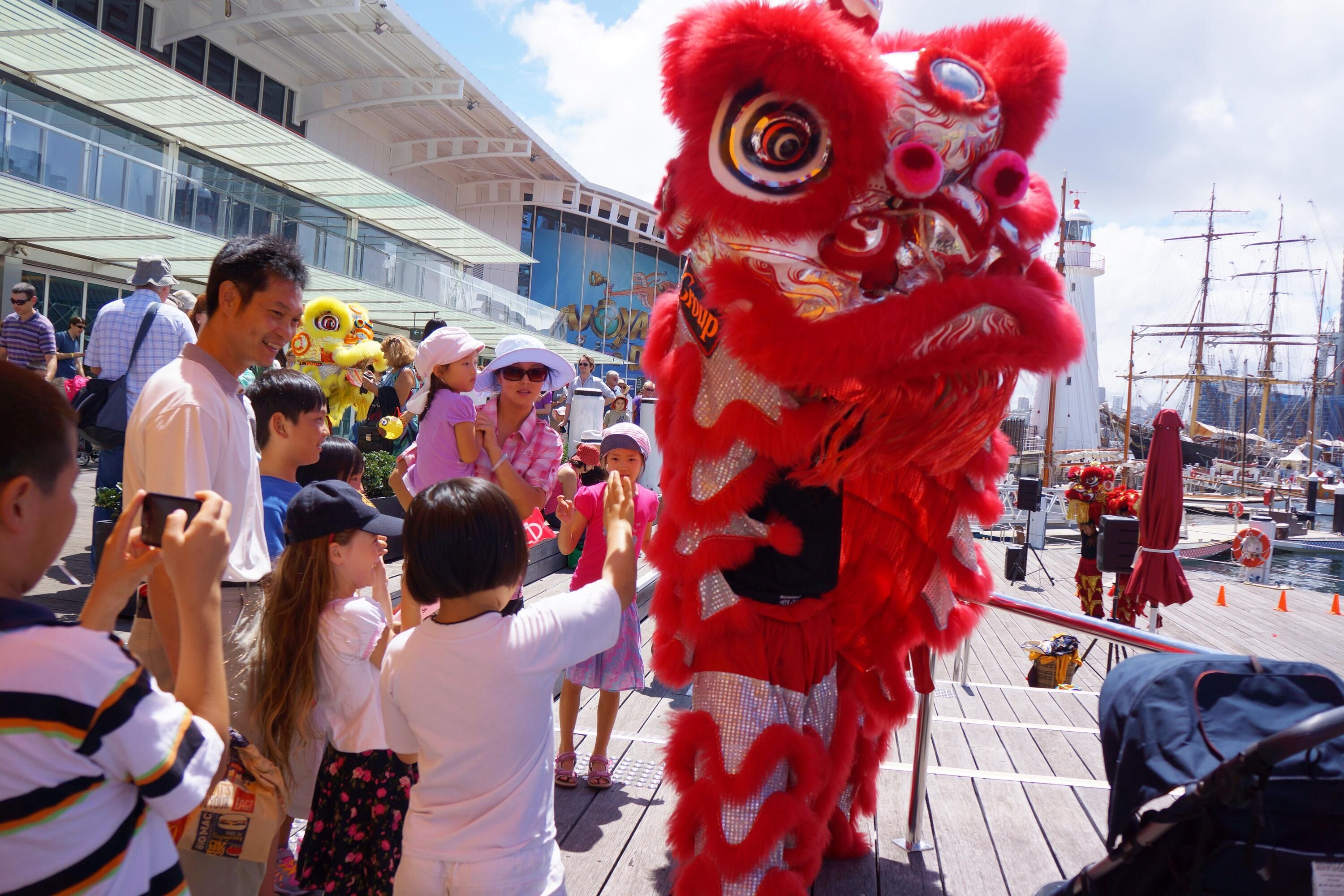 Photo showing a Red Chinese dragon costume outside the museum with several families around it. 