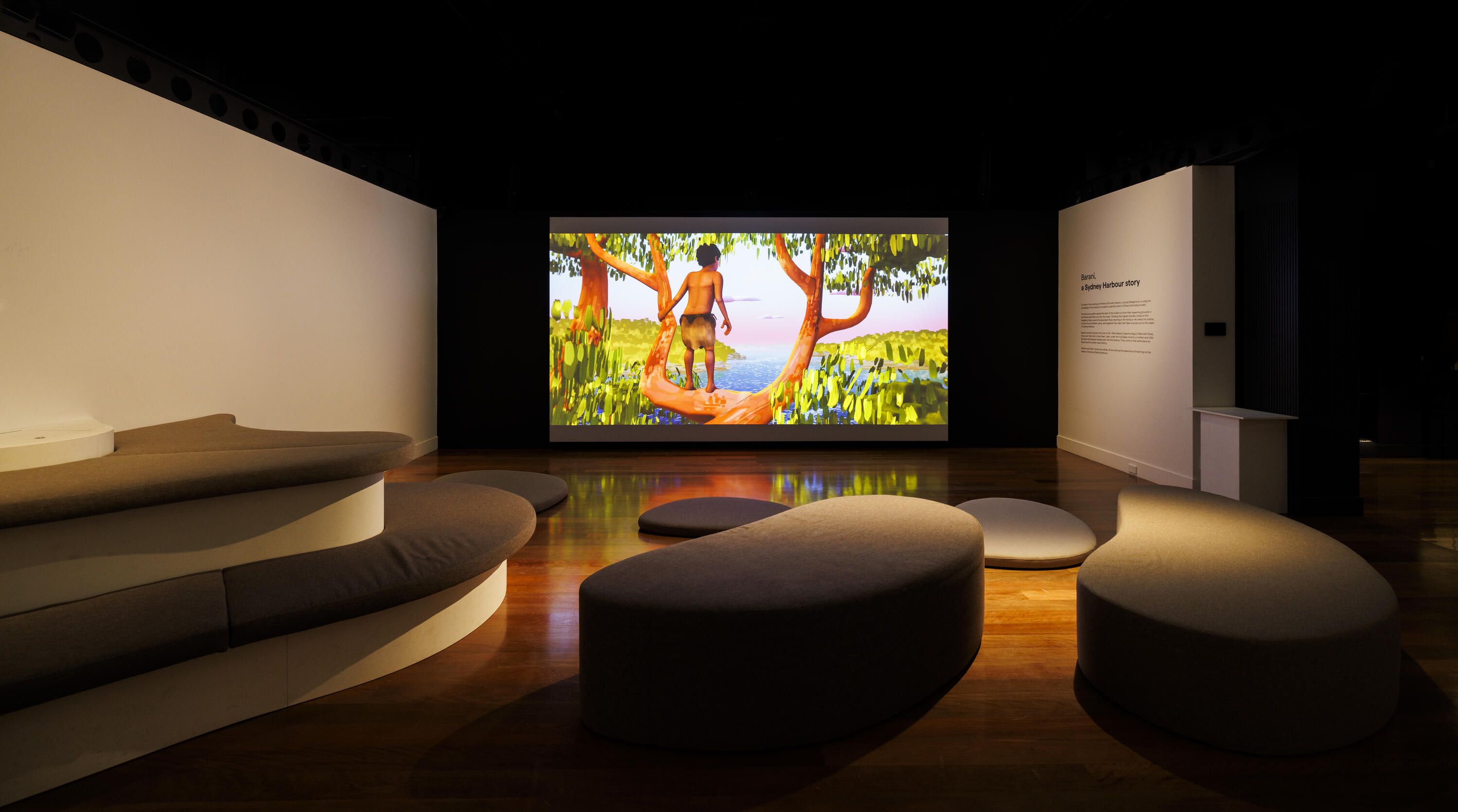 Photo of a museum exhibition space with curved soft seating and a large projection screen