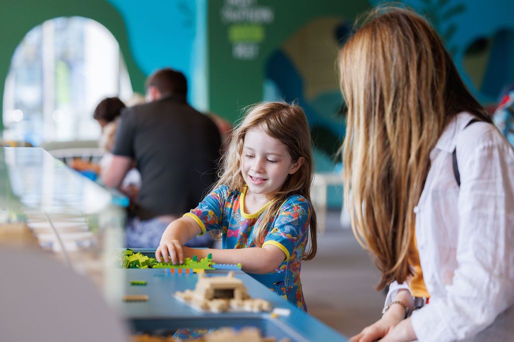 Photo of a girl building with Lego while a woman, her mother, watches