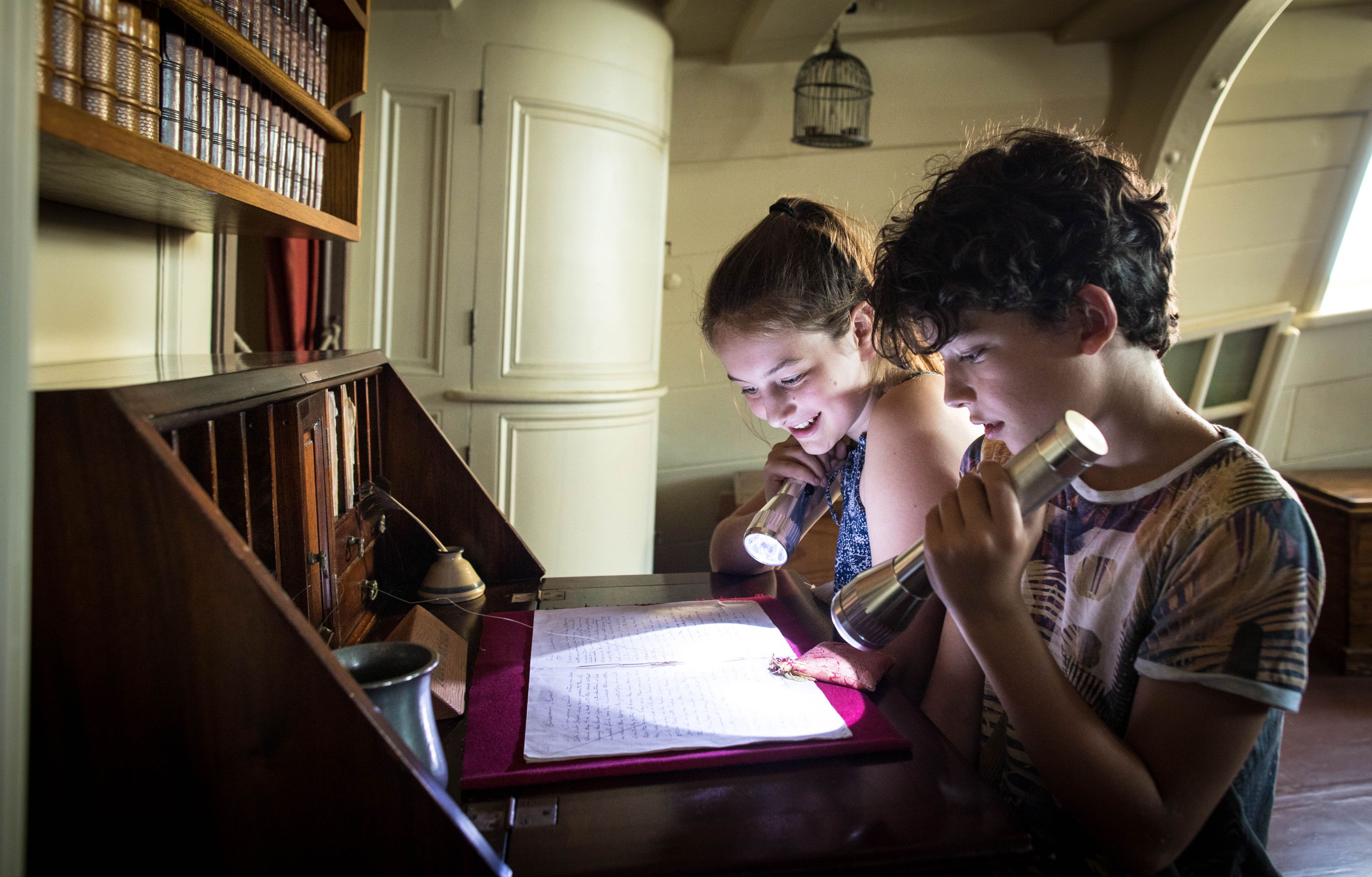 2 children using torches to look at a letter on an old fashioned desk.