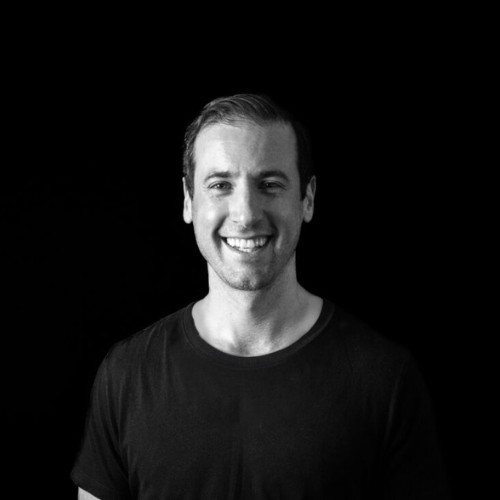 Black and White Photo of a smiling man with light skin, dark hair and wearing a black t-shirt.