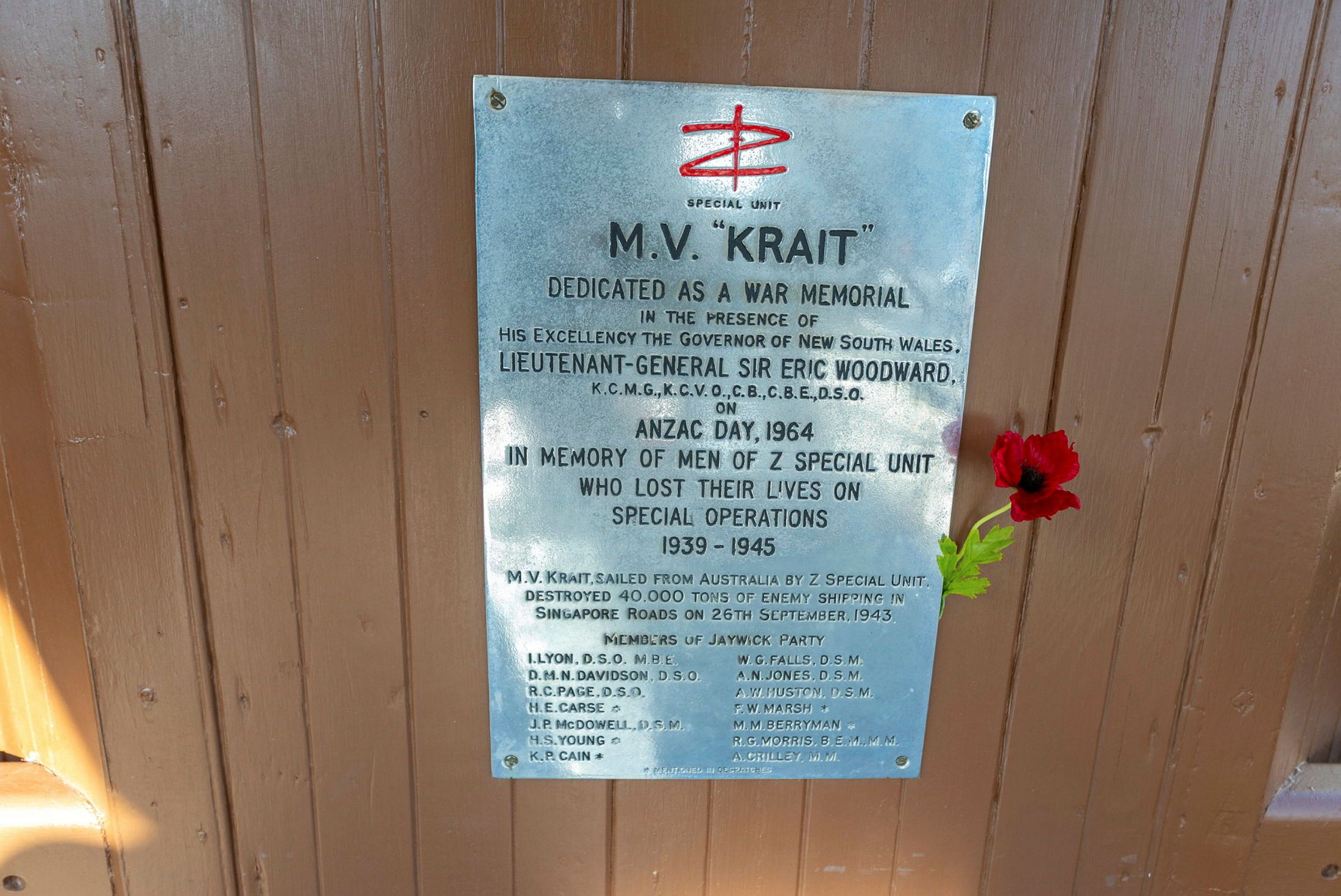 Photo of a silver plaque onboard MV Krait, with a red poppy next to it.  