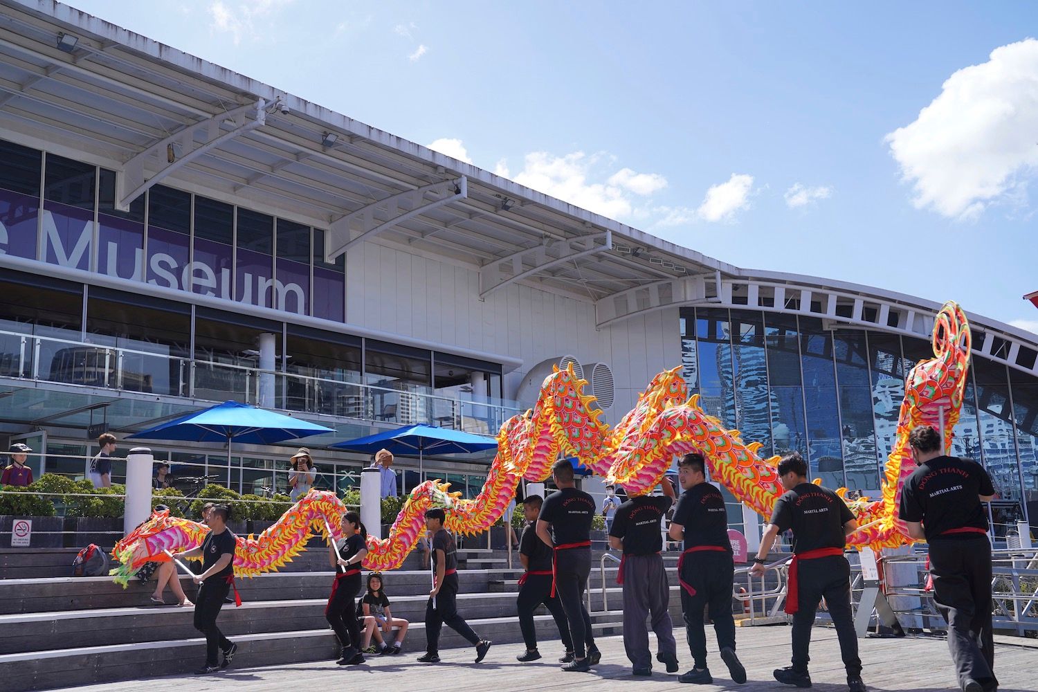 Photo of a colourful, Chinese dragon puppet controlled by a group of people wearing black. 