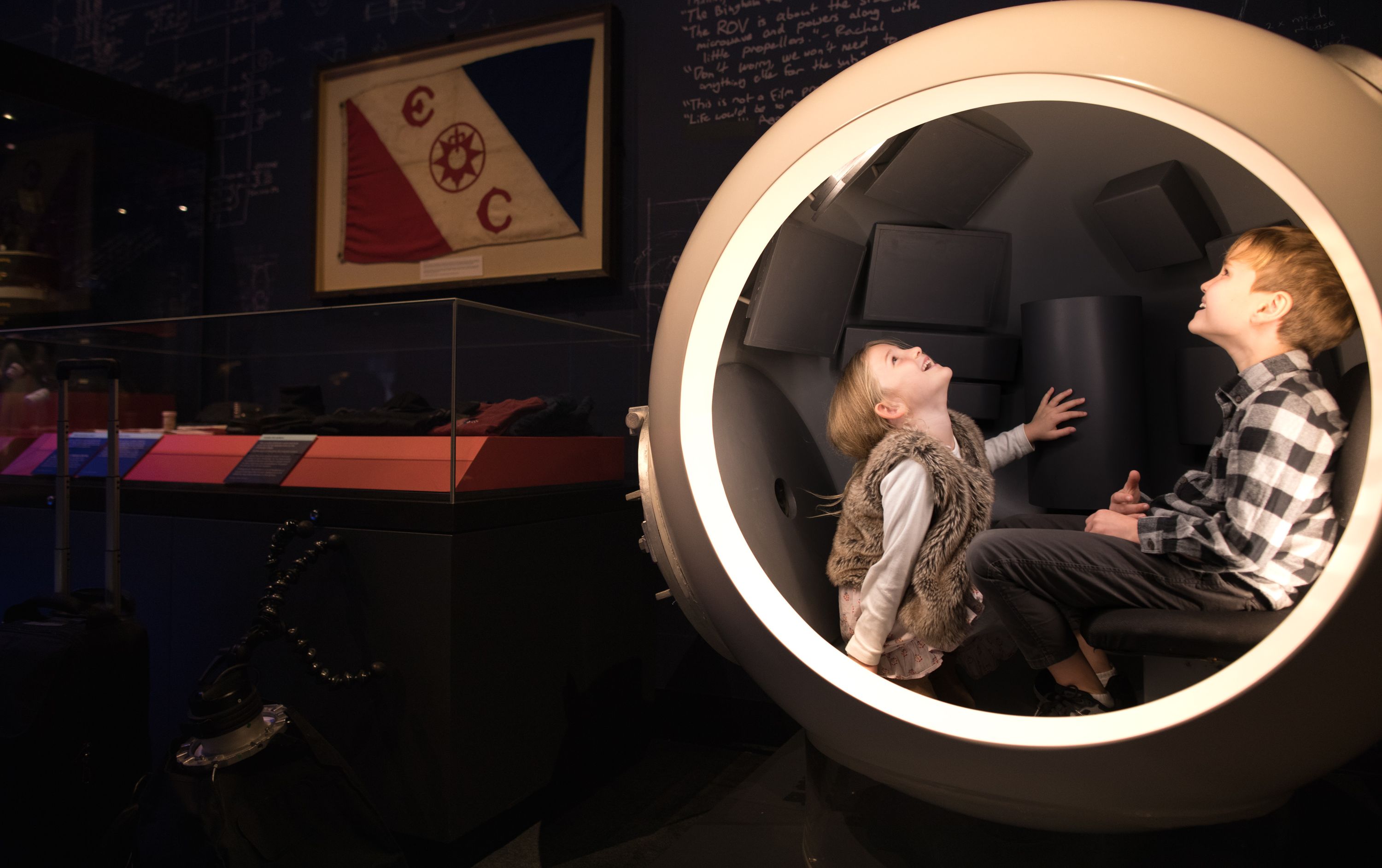 Photo taken inside an exhibition of two children in a round sphere looking up.