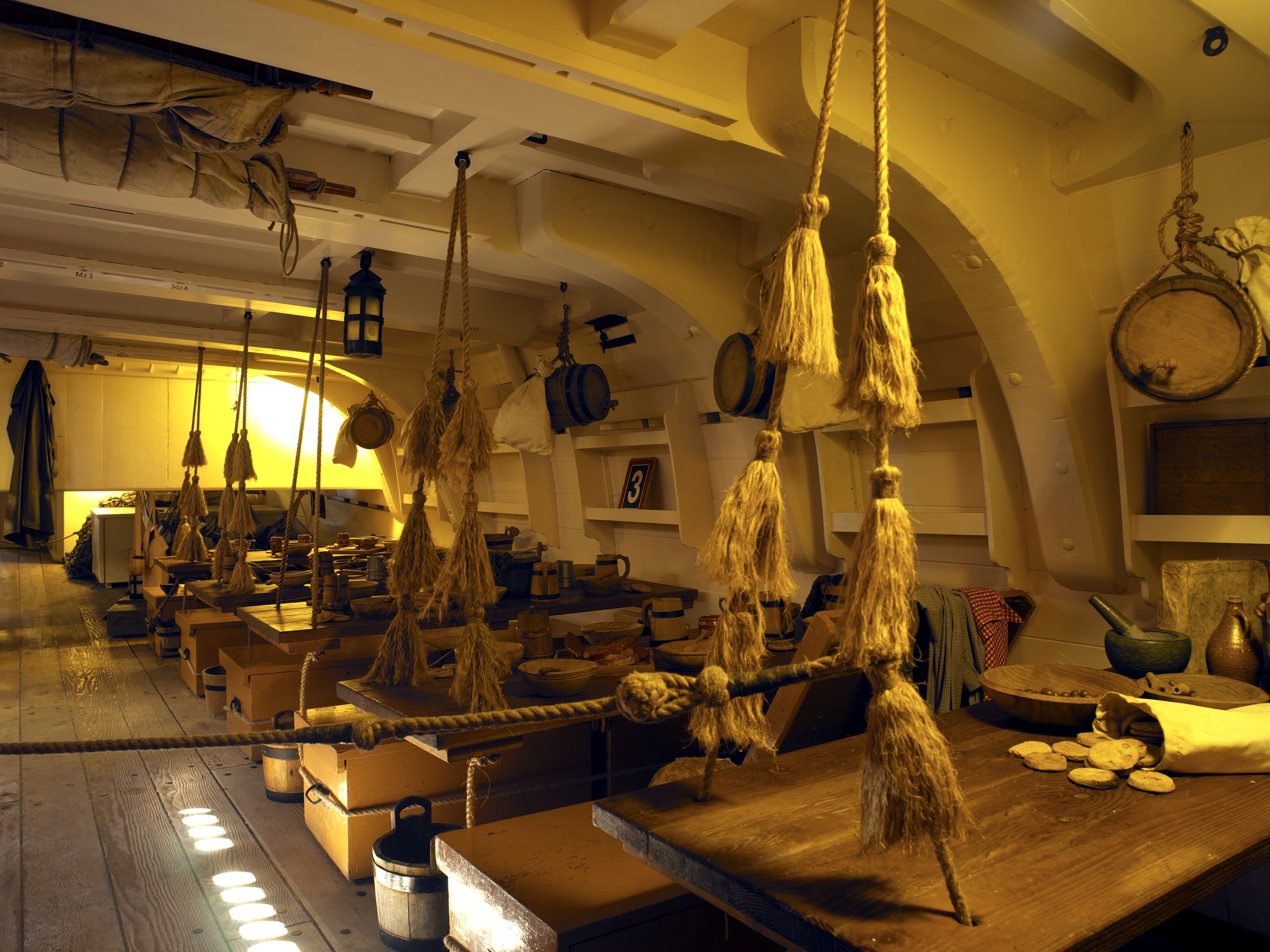 Photo showing below decks on a wooden tall ship, featuring a row of tables. 