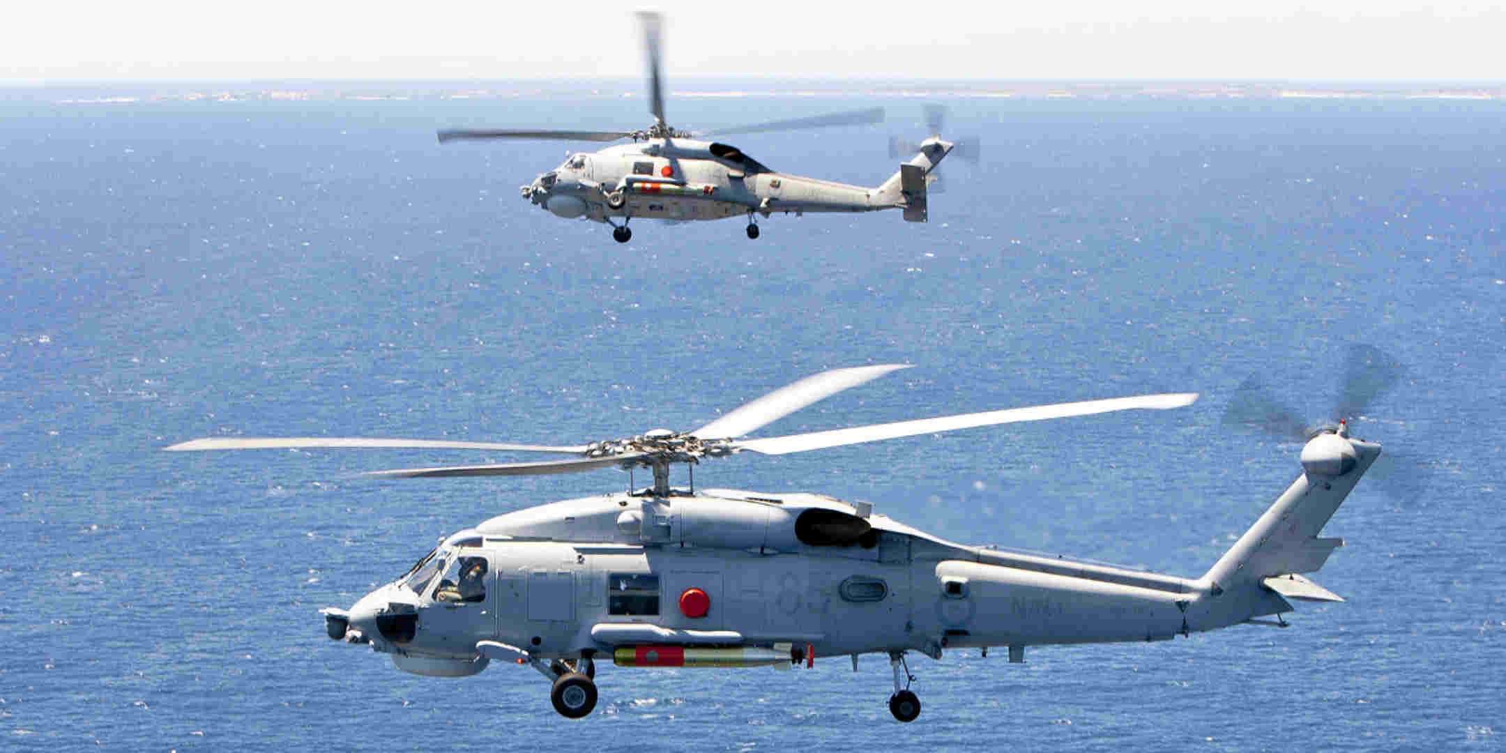 A photo of two navy helicopters flying over the ocean.