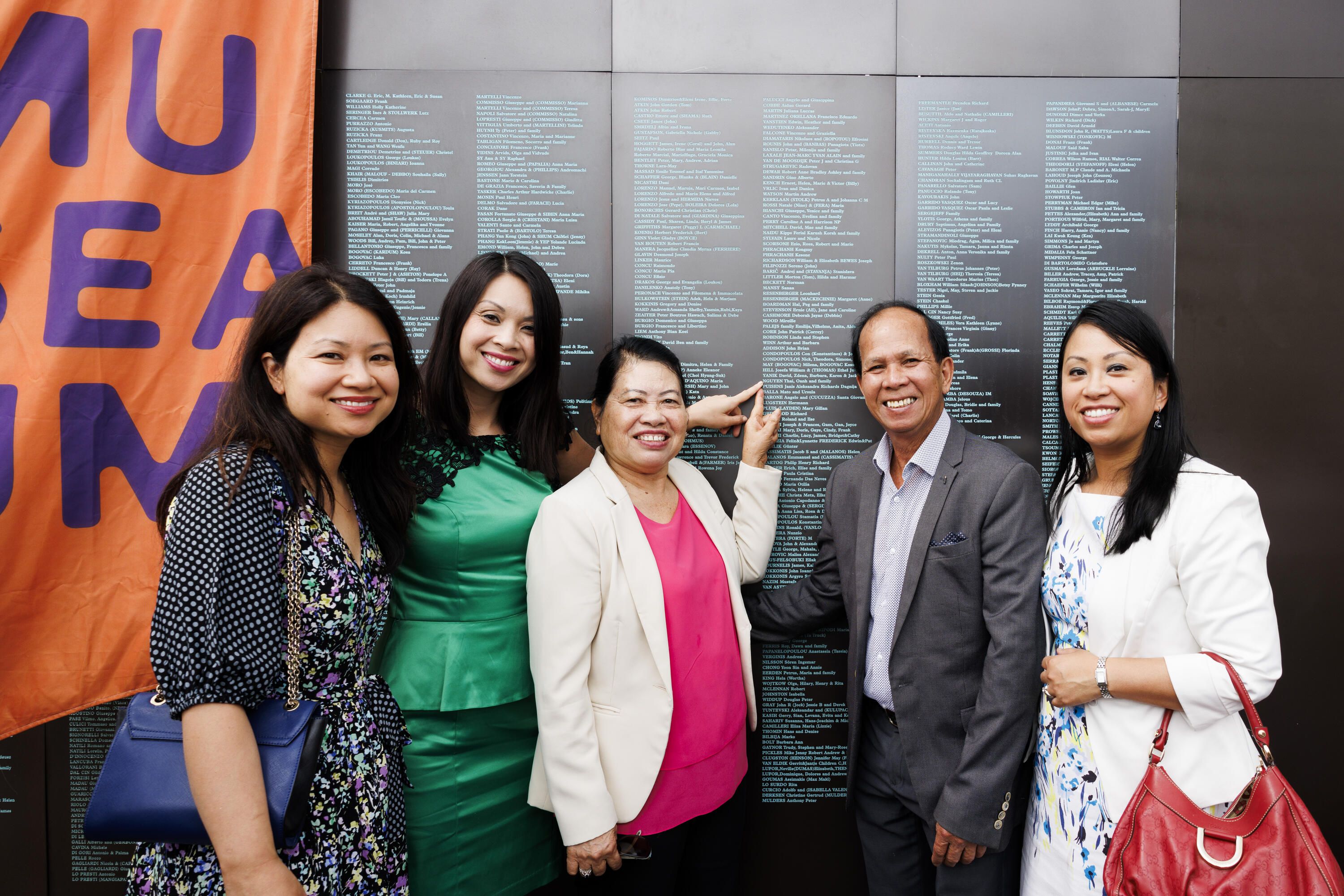 Group of 5 people in front of a wall, pointing at inscriptions 