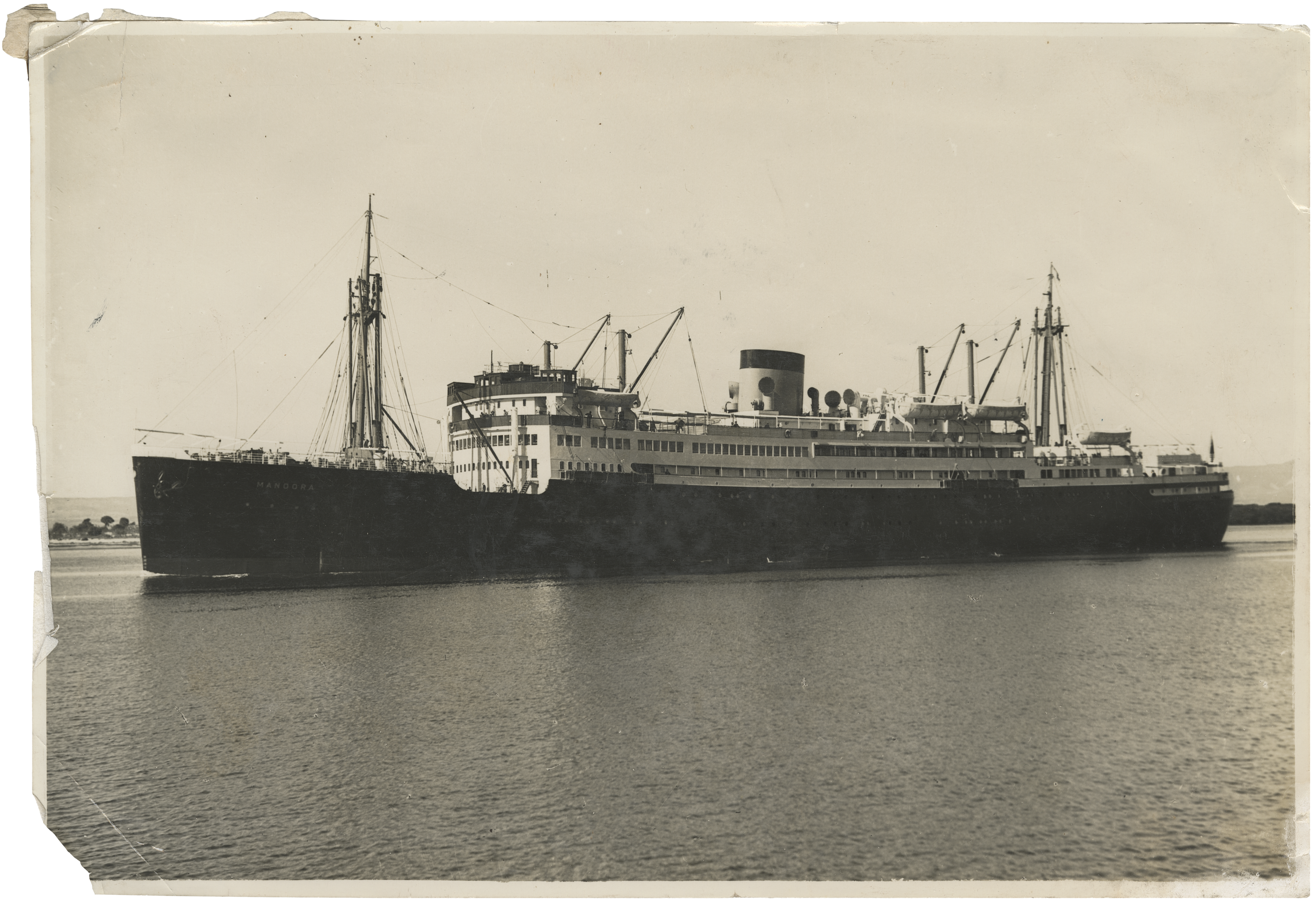 Black and white photograph showing a ship with a dark hull and white upper decks, with cranes on the deck.