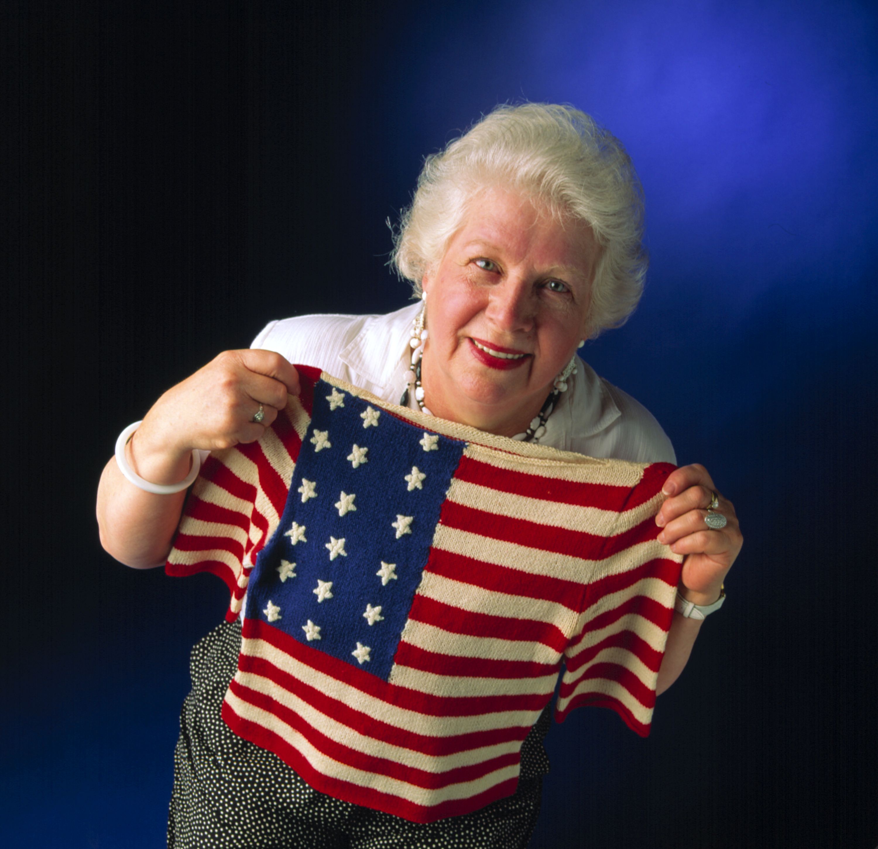 Woman with white hair holding a hand knitted jumper with the American stars and stripes flag.