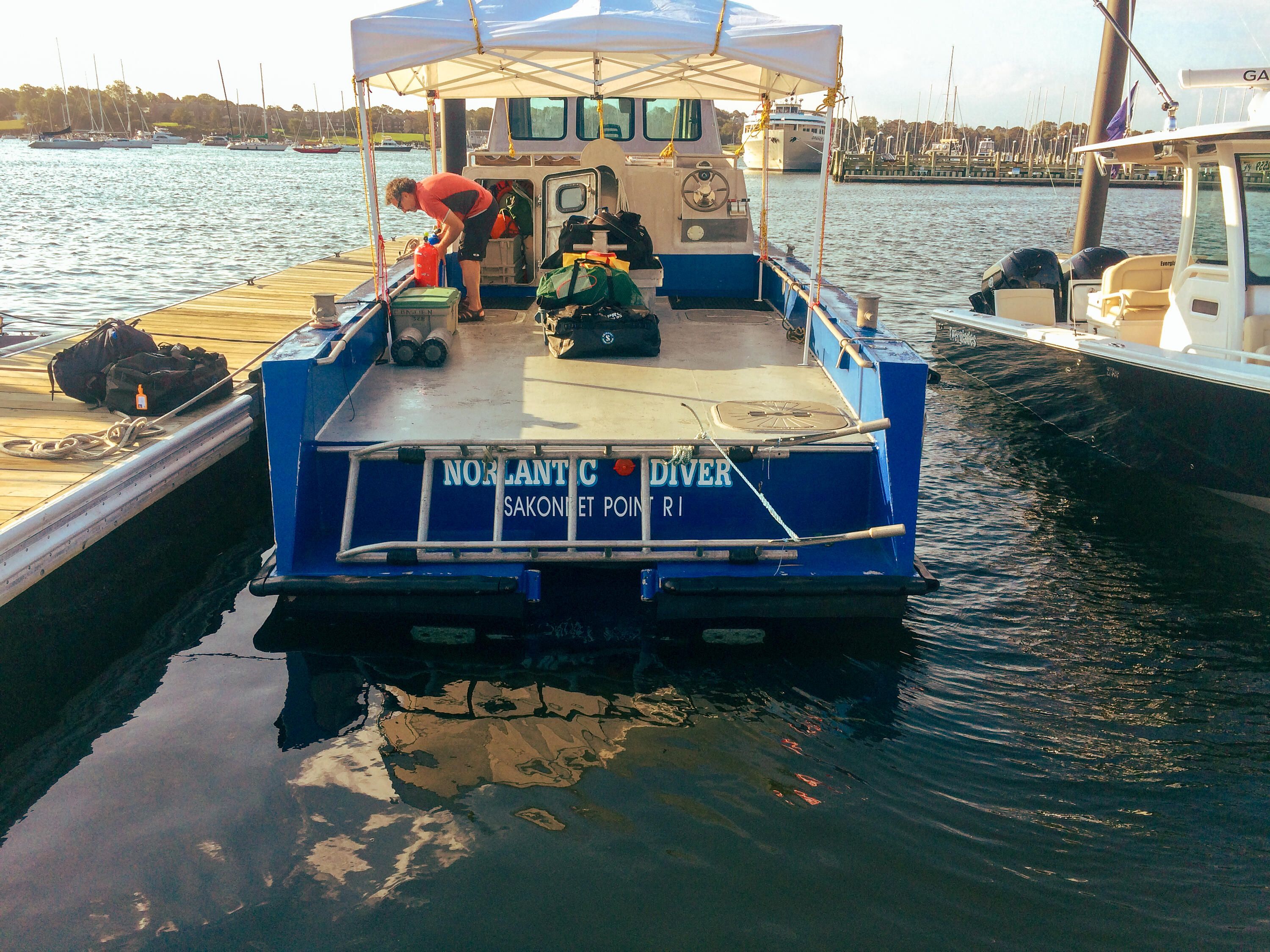 A photo showing a boat at a wharf, with several people organising gear and getting ready for a dive.