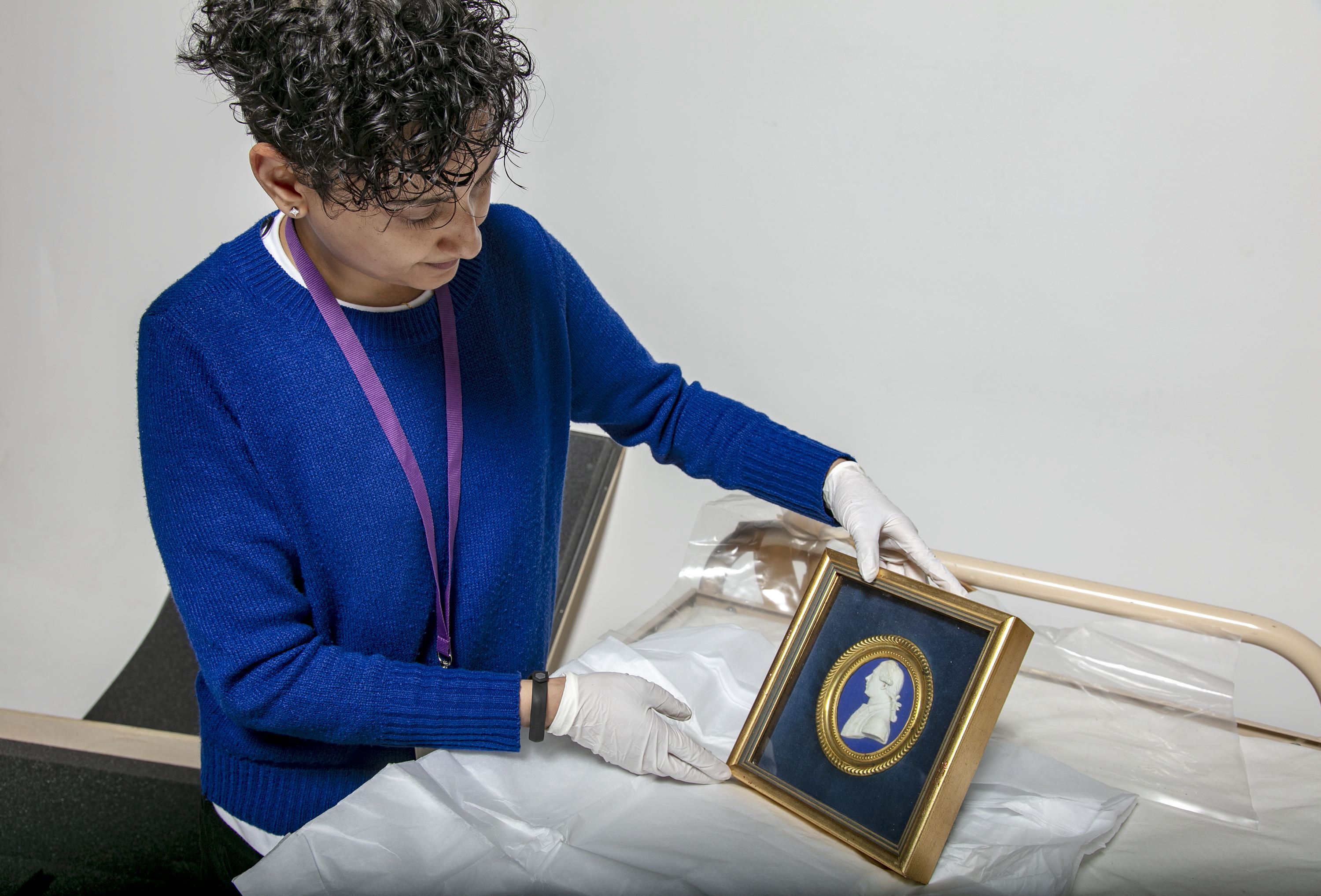 Photo of a museum staff member carefully holding a framed object.