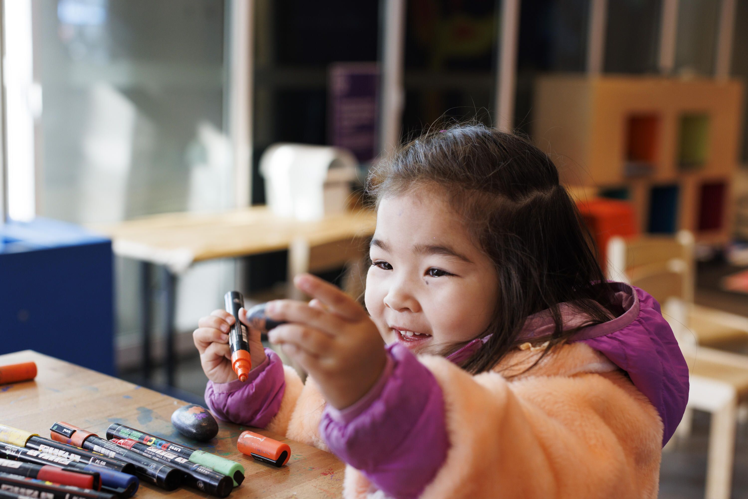 A little girl uses paintpens to decorate a rock.