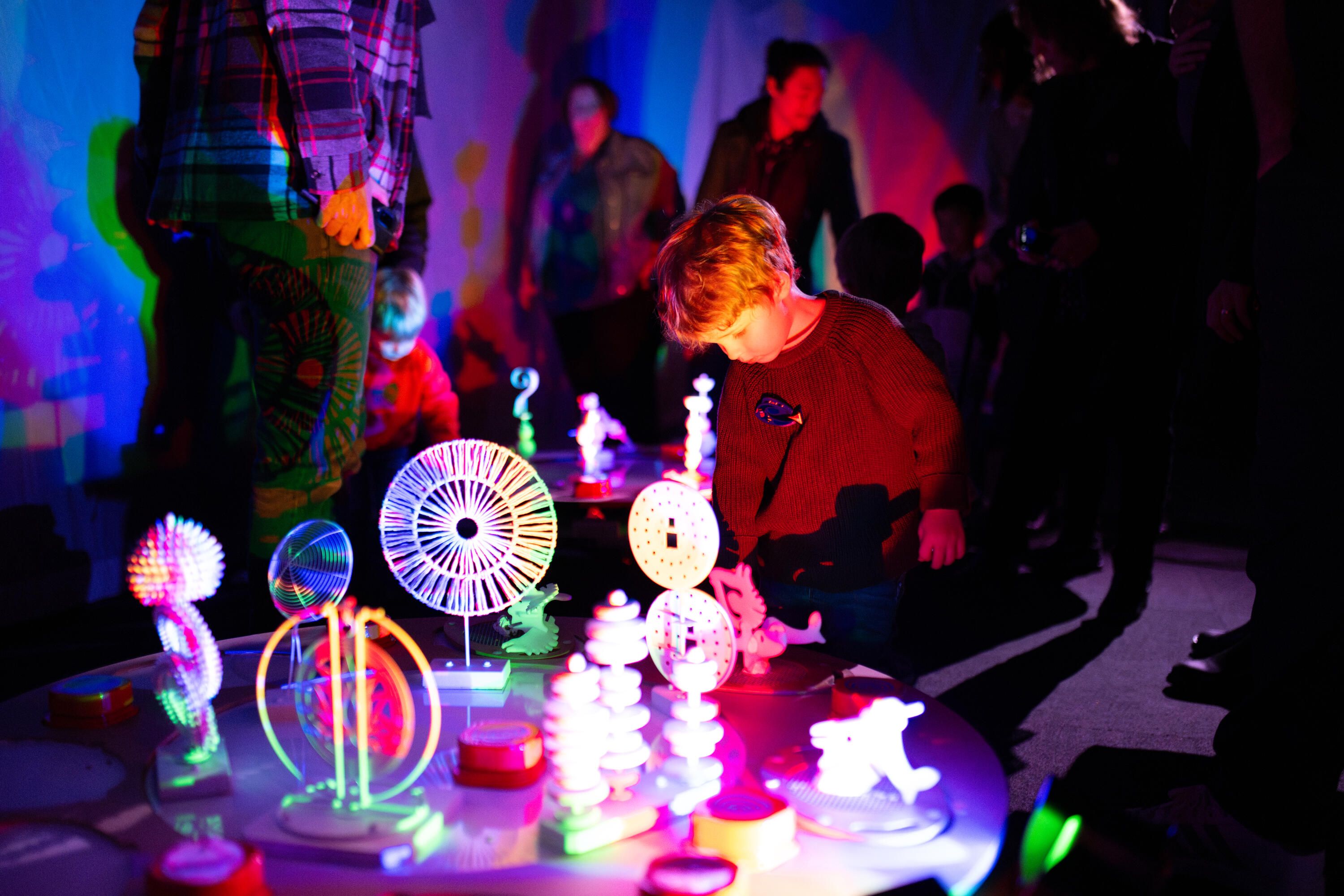 Children playing with interactive theatre props in colourful light.