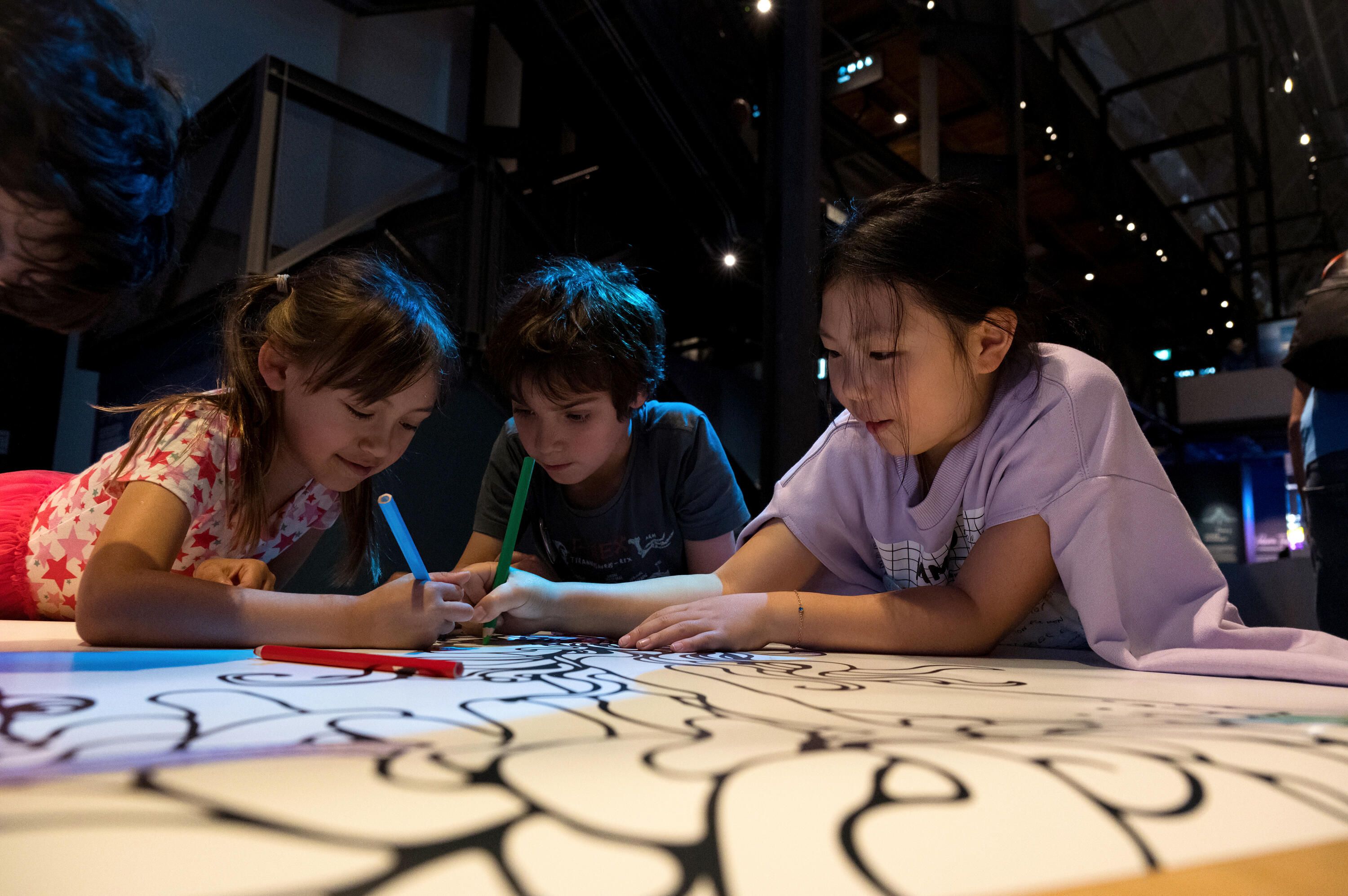 Photo of 3 children, 2 girls and a boy, colouring a large scale colouring in sheet 