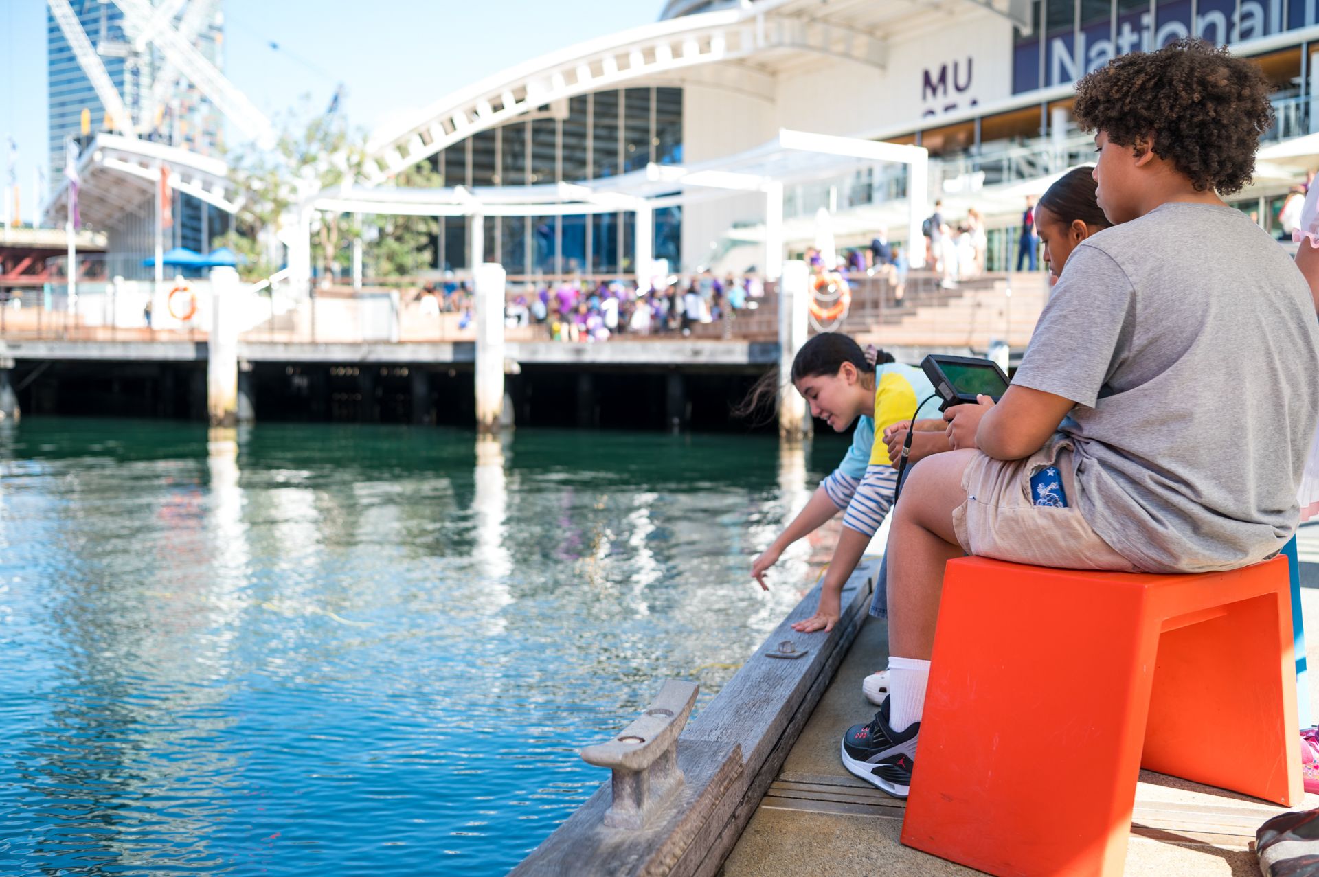 Photo showing two children and a museum staff member using a remote control to drive a robot in the water.