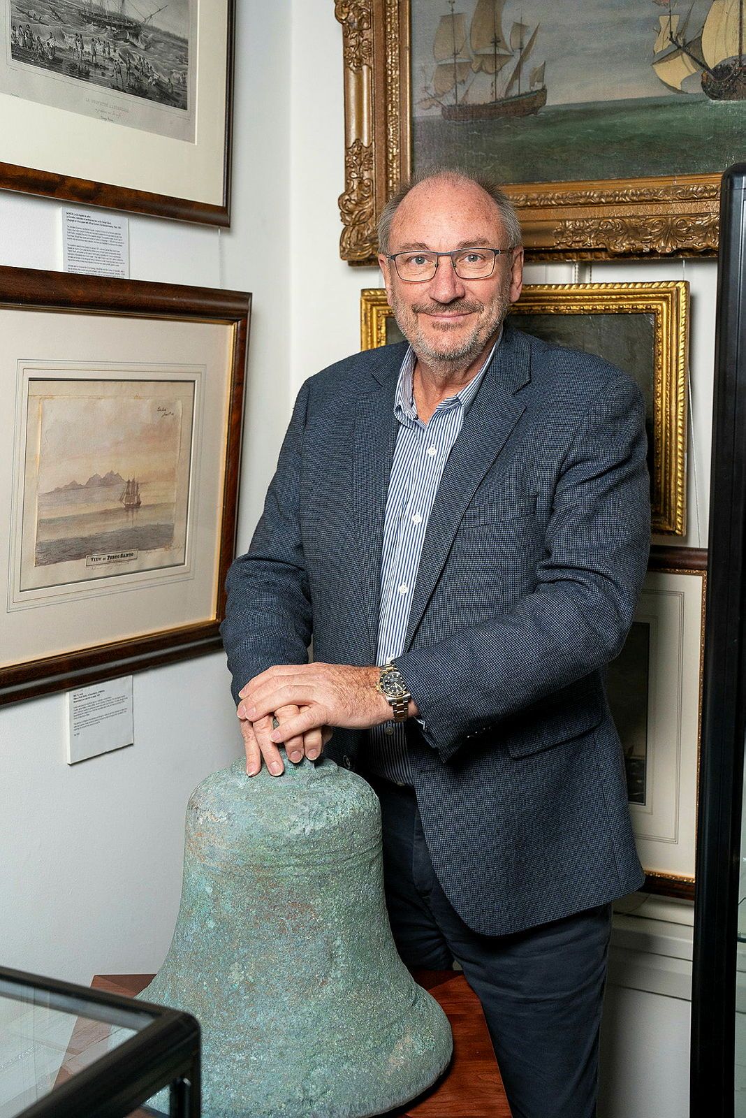 Photograph showing a man standing in a gallery with a large, green, metal bell