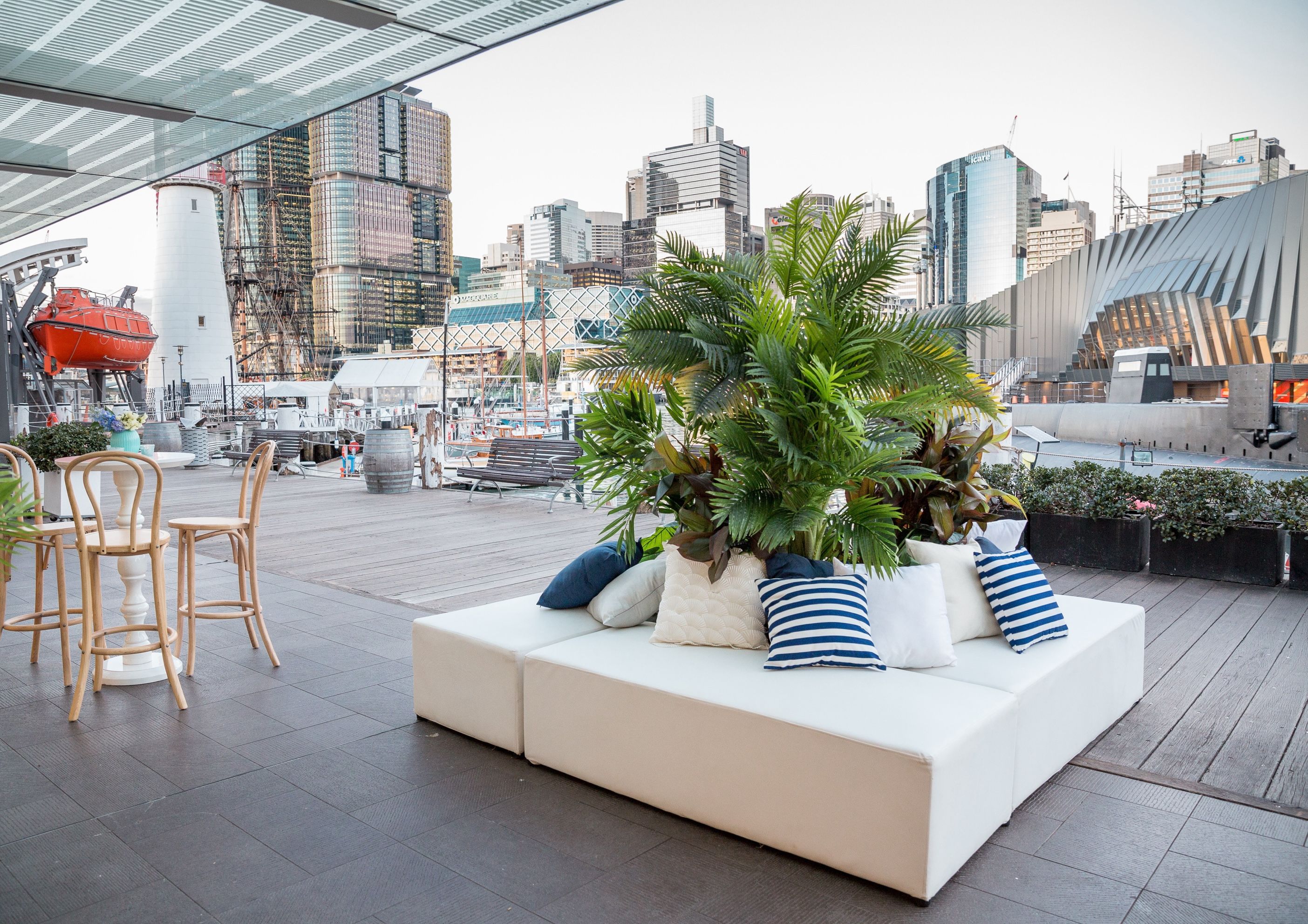 Photo showing an outdoor space with seating and plants, with the harbour and city in the background.