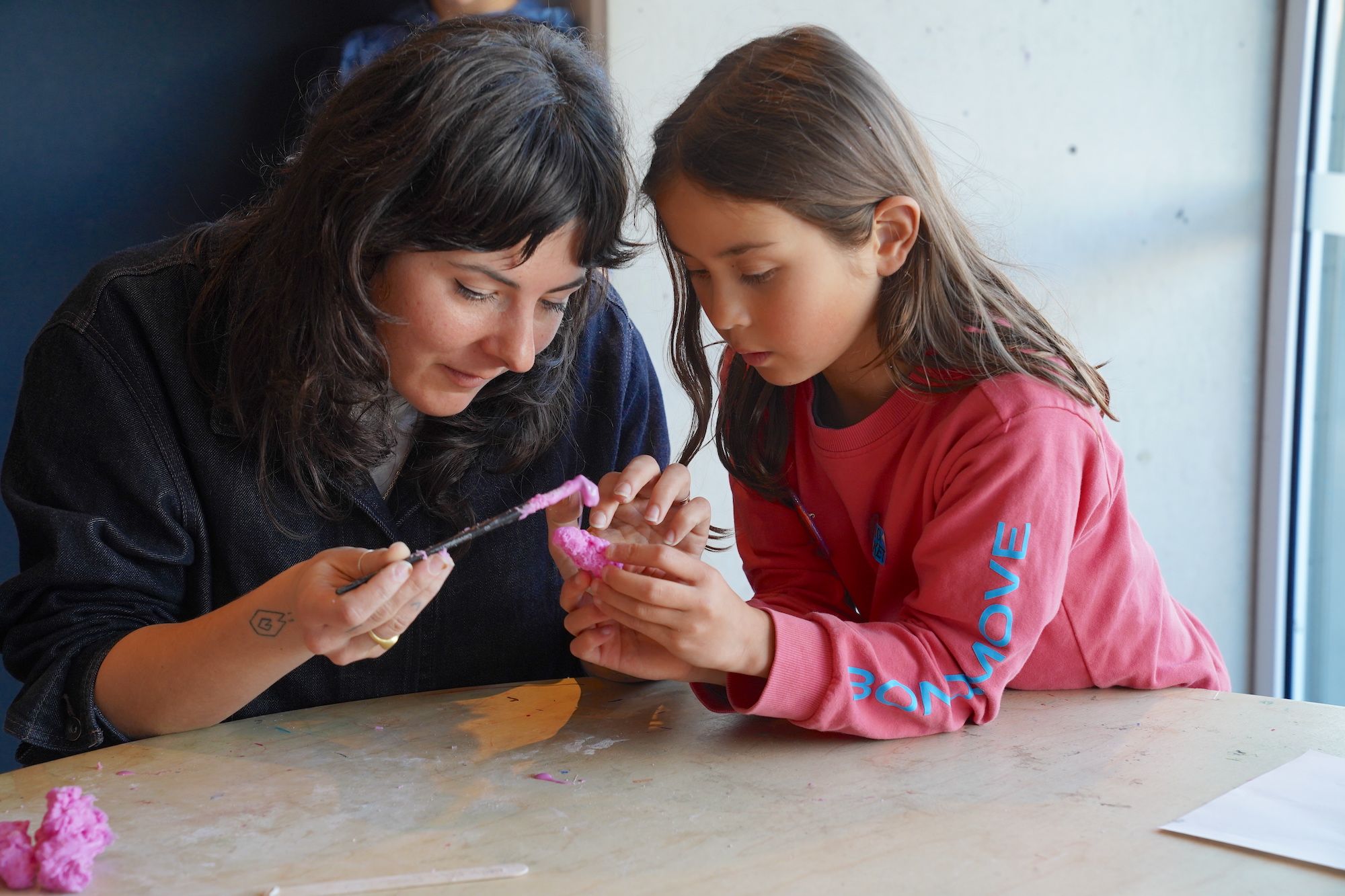 A girl in a red top with an adult woman wearing black, working together on a craft activity.