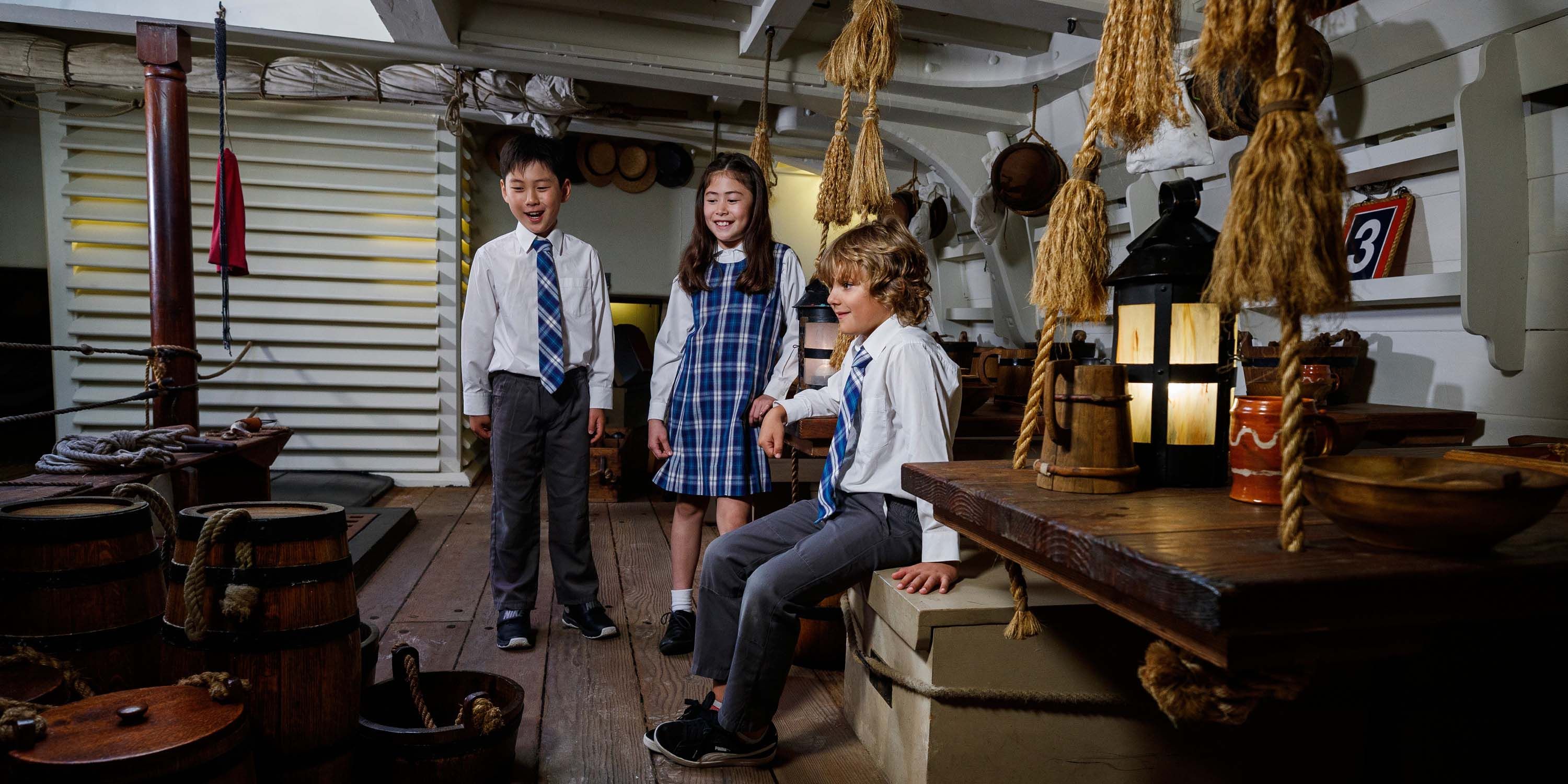 School kids exploring below decks of ENDEAVOUR. Two boys and a girl check out the ship's mess.