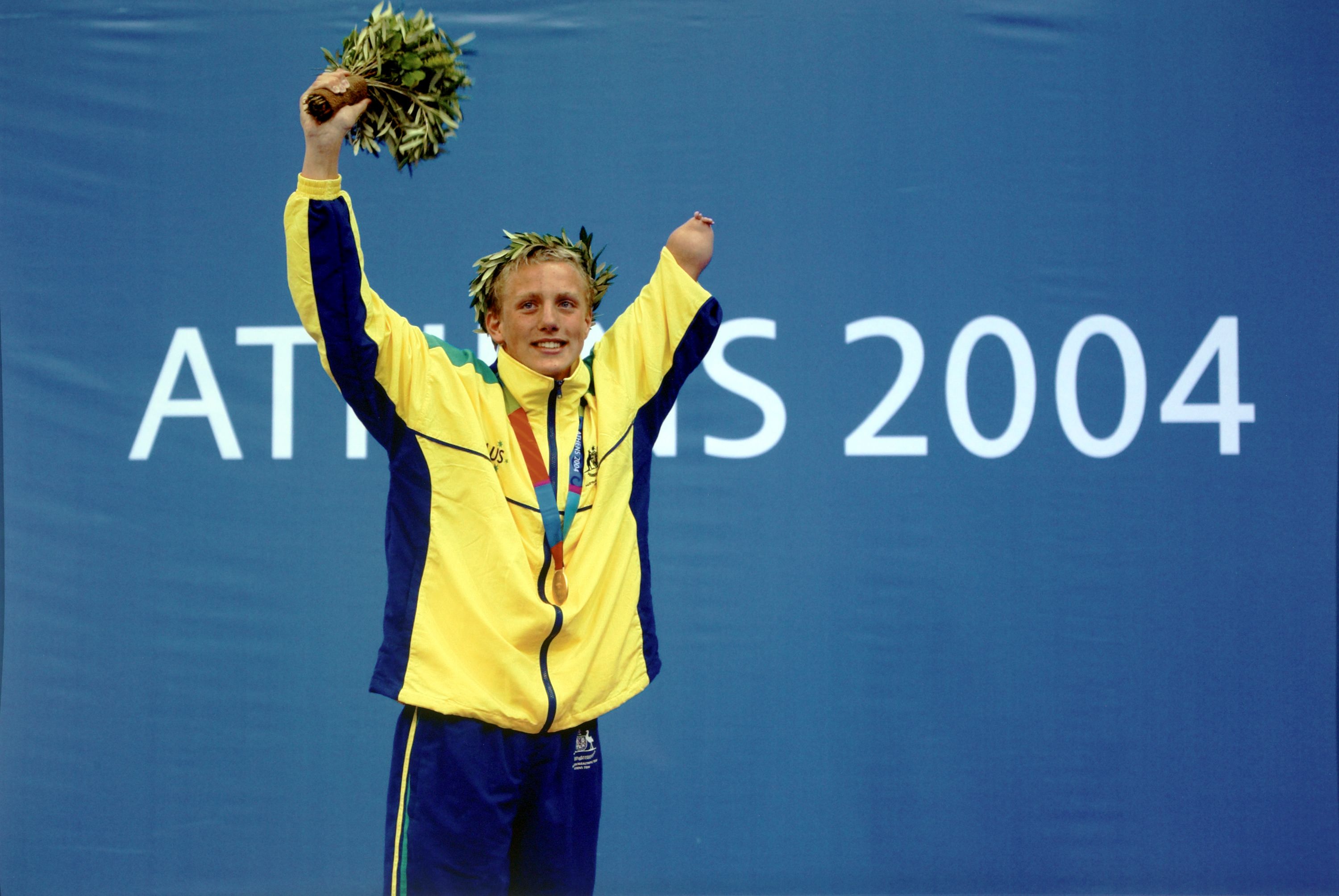 Photo of a male, Paralympic athlete on a winners podium. The wall behind him says Athens 2004.