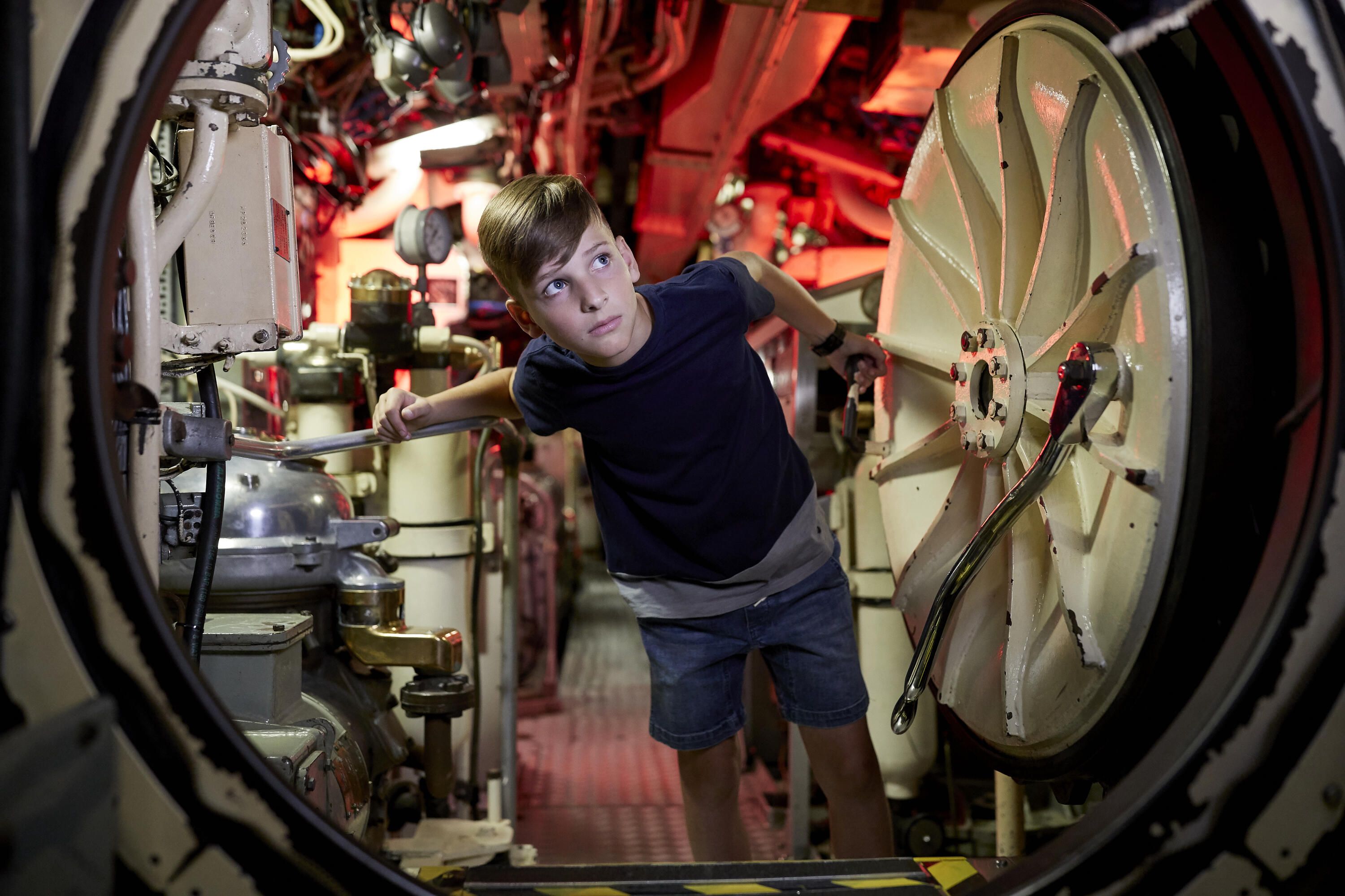 Photo of a round hatch on a submarine with a boy looking through.