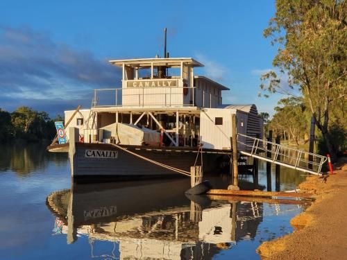 Photo of a boat, a paddle steamer, on a river alongside the bank.