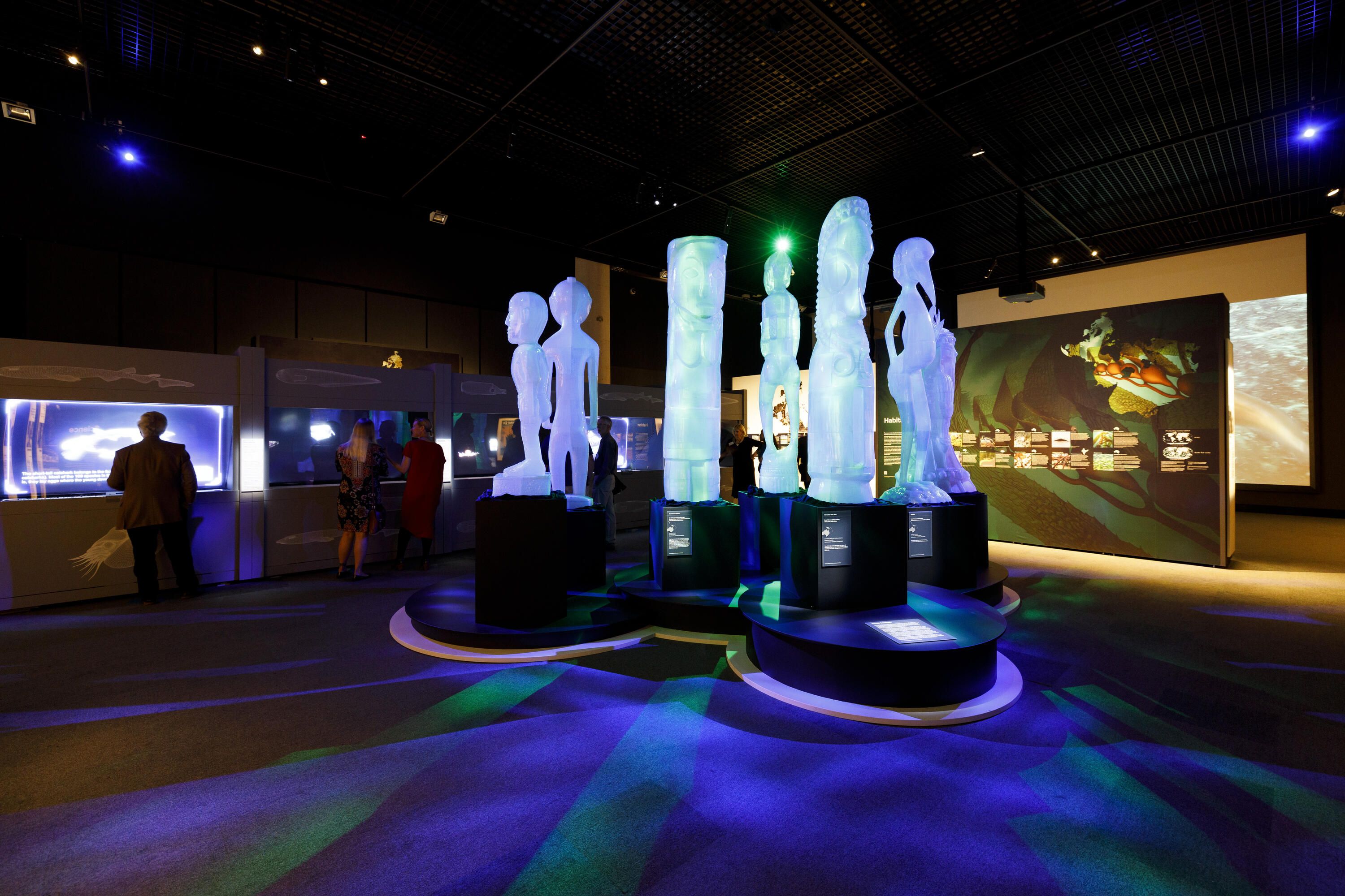 Photo of a dark, museum exhibition featuring large white sculptures.