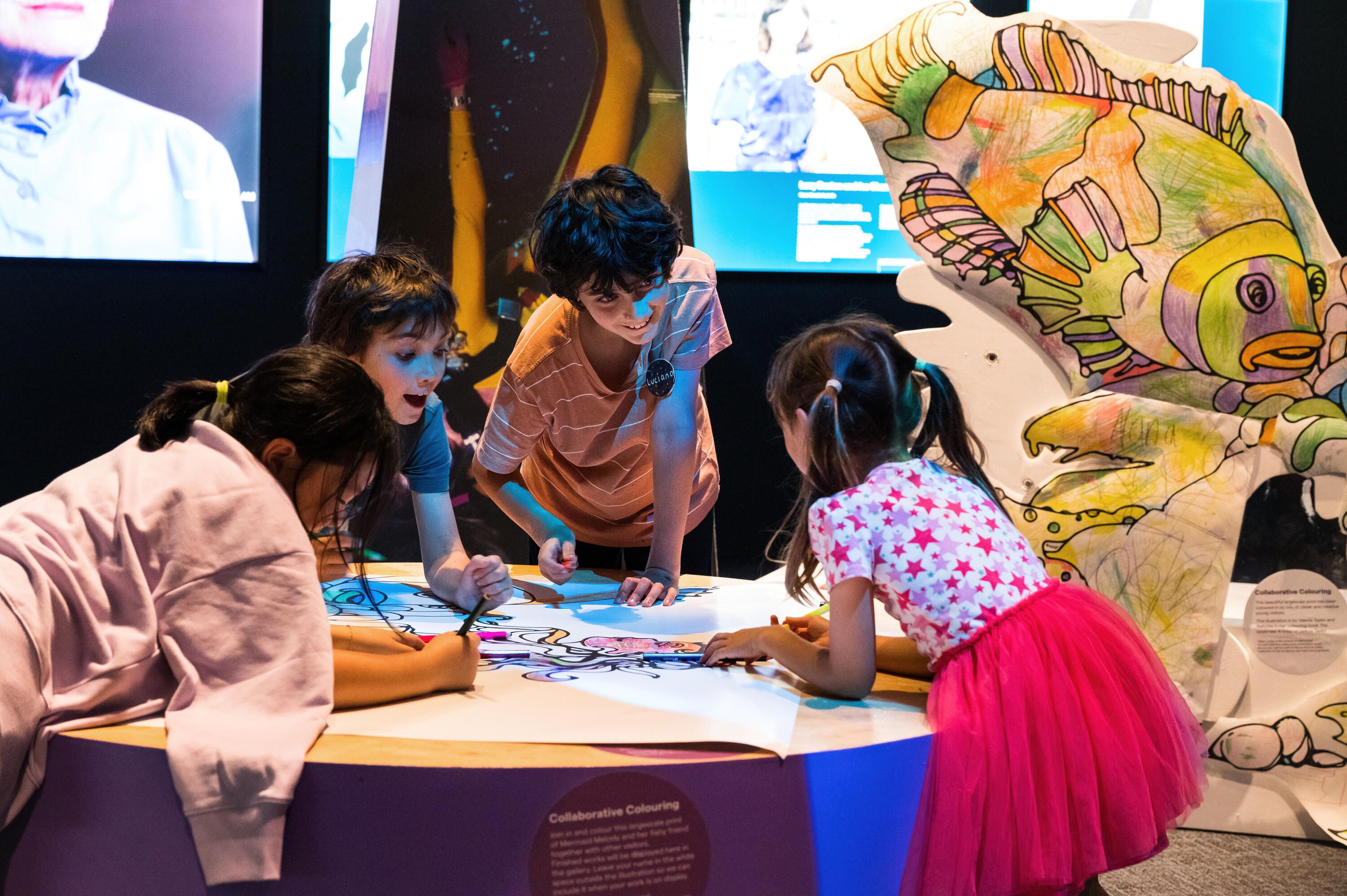 Photo of 4 children, colouring a large scale colouring in sheet 