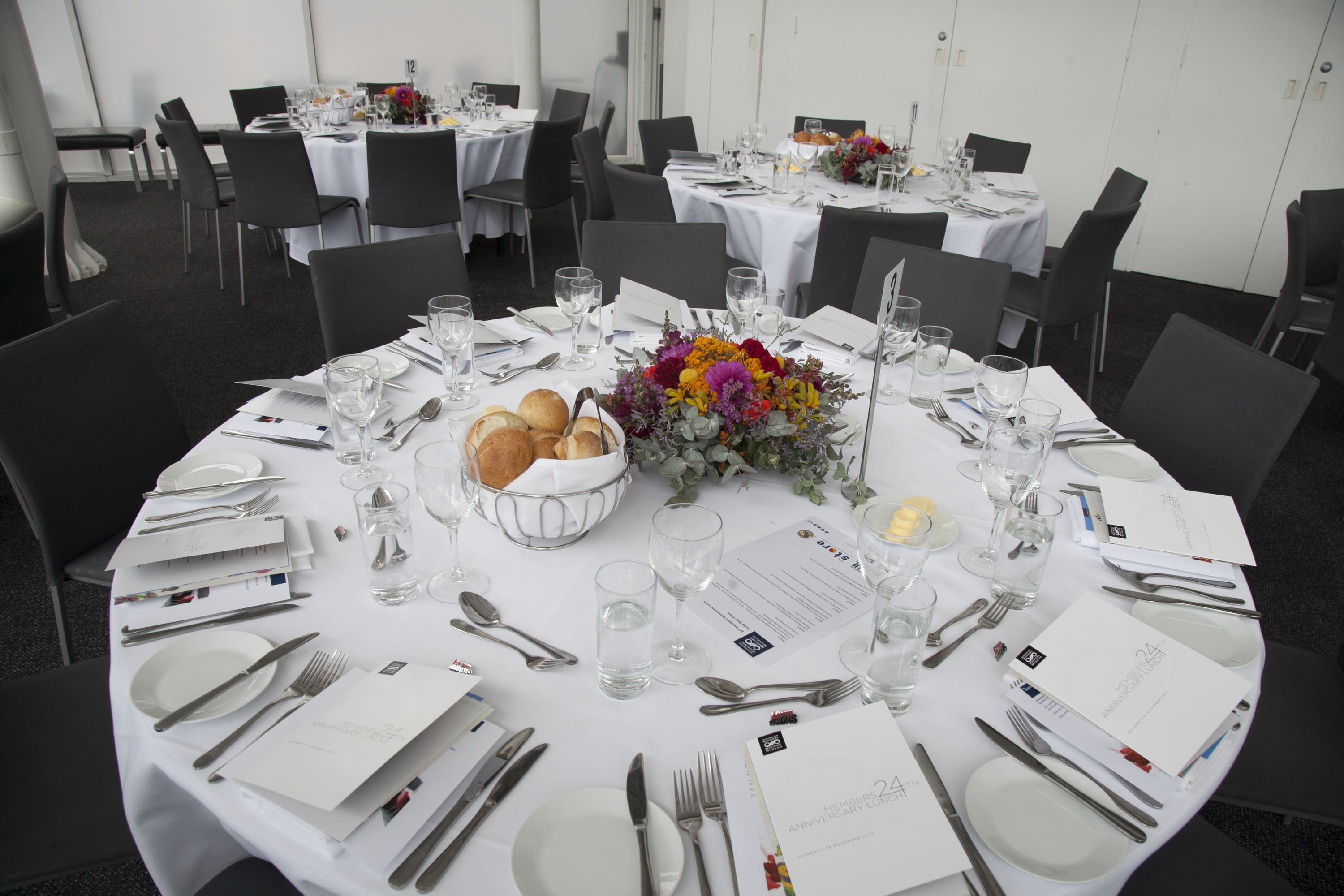 photo of a large round table set with a white tablecloth for a formal event with flowers in the centre. 