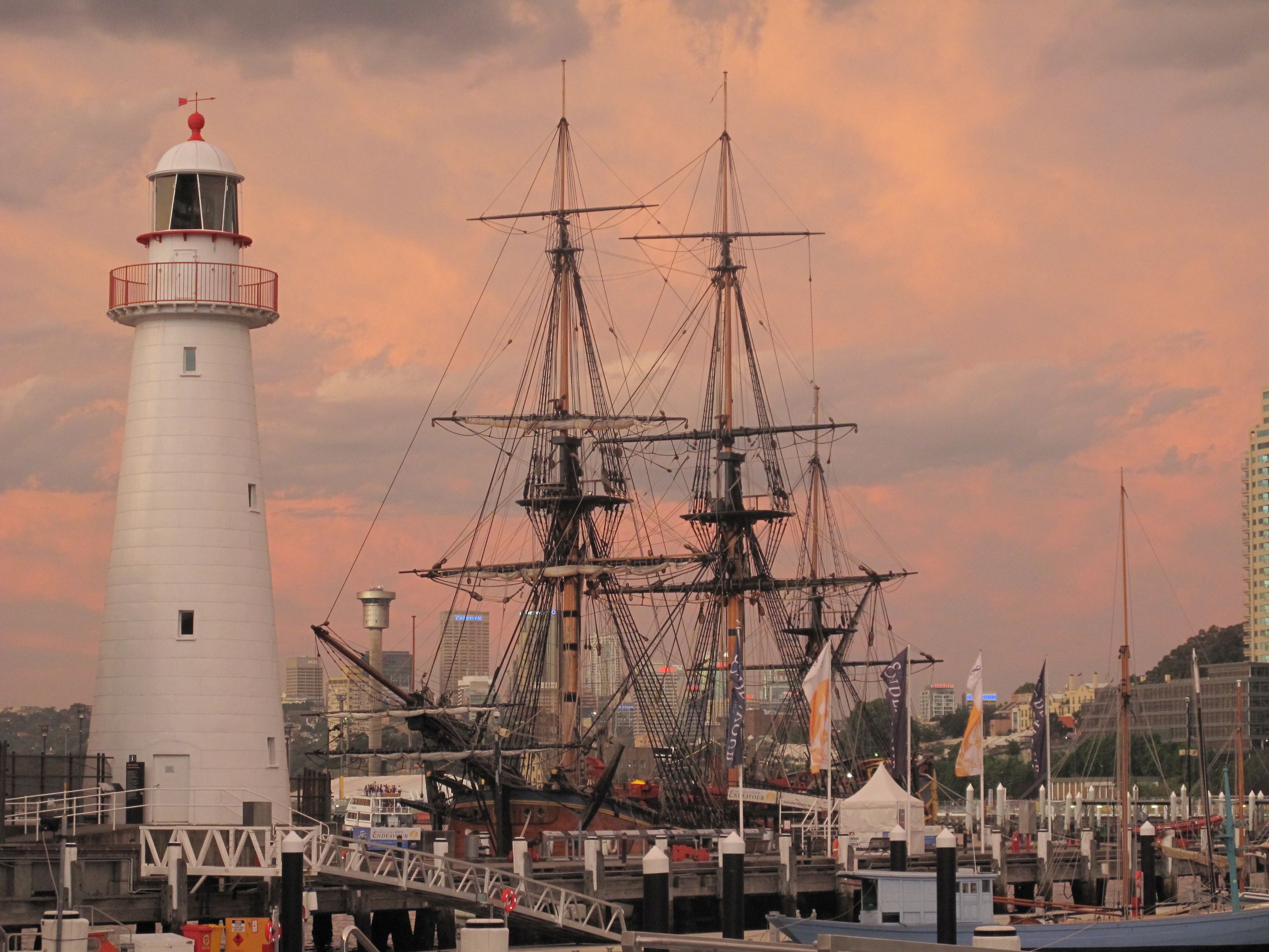 Photo of tall ship and lighthouse, with a pink orange sunset.