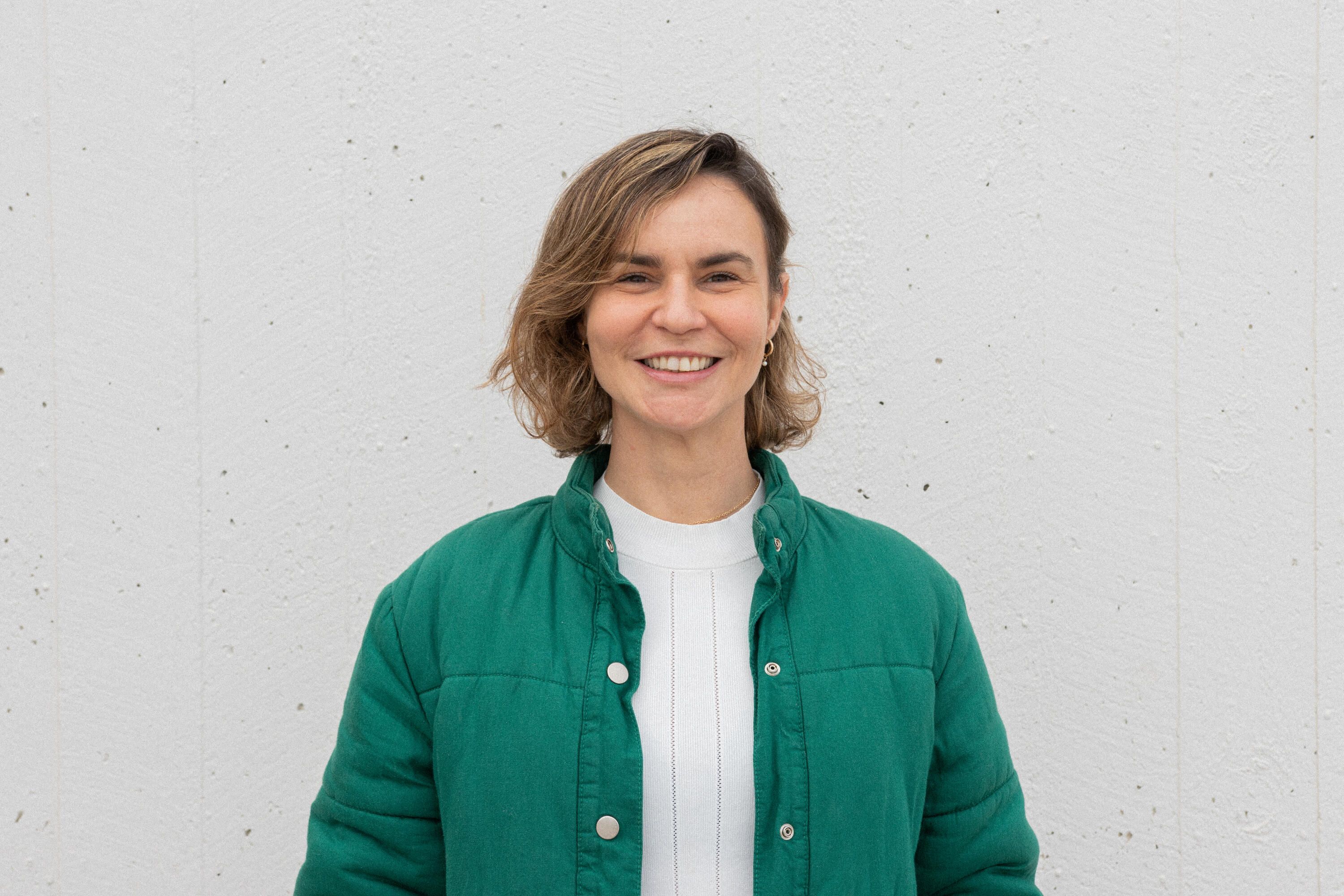 Photo of a woman with short brown hair wearing an unbuttoned green shirt over a white top.
