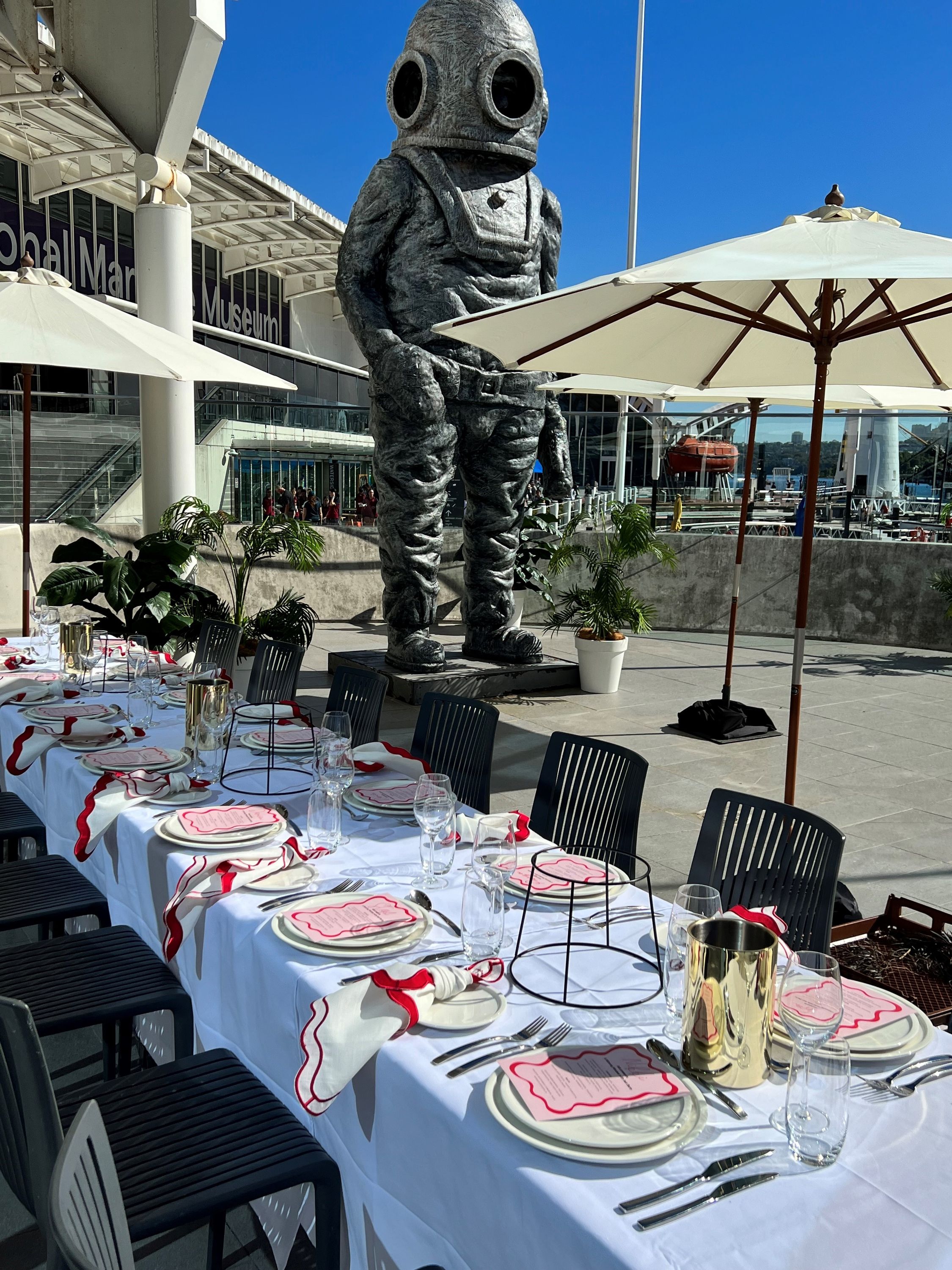 photo of a table and place setting on an outside balcony, with an umbrella and a statue in the background