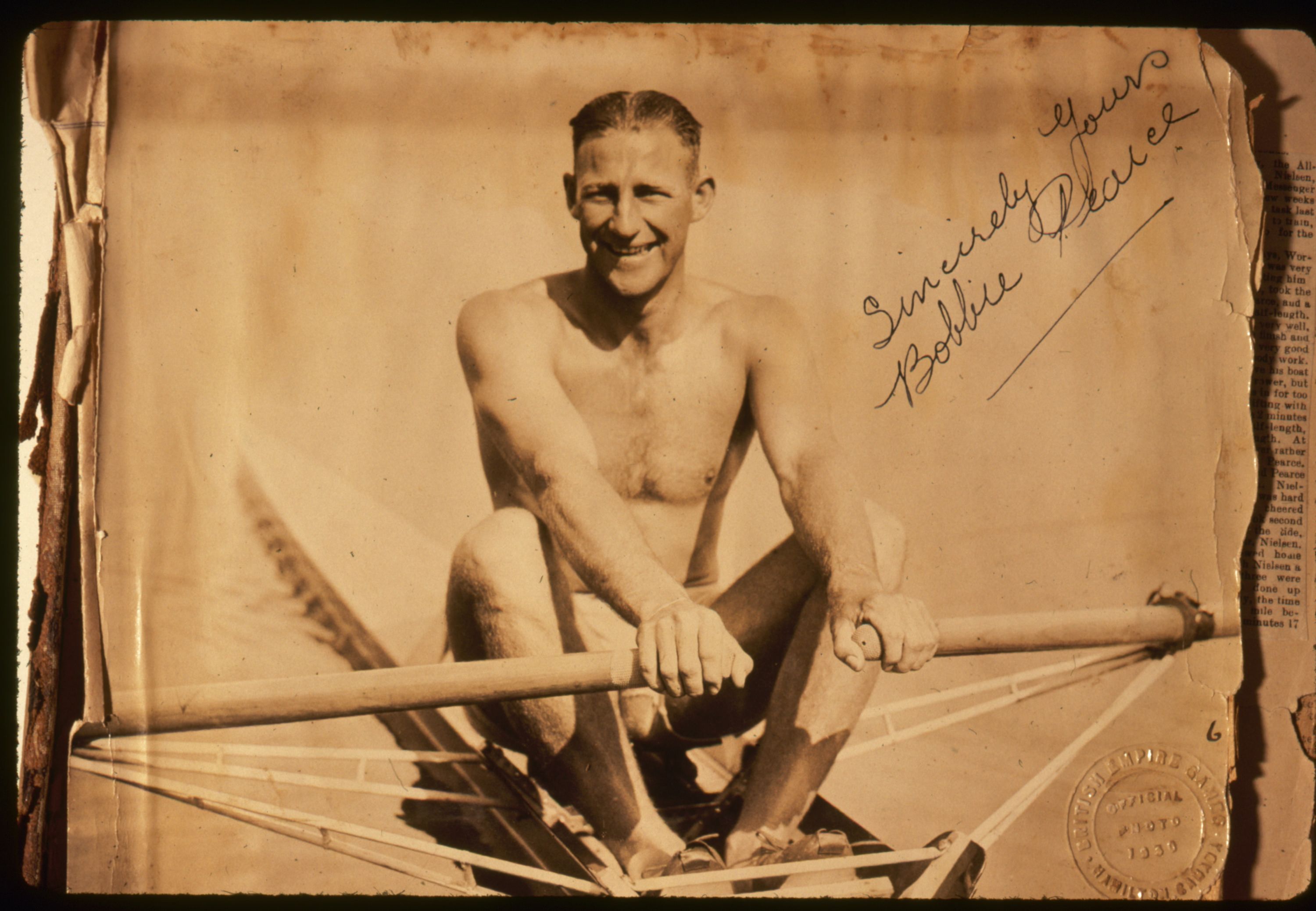 Black and White photo on very yellowed paper of a shirtless man with short hair in a row boat. 