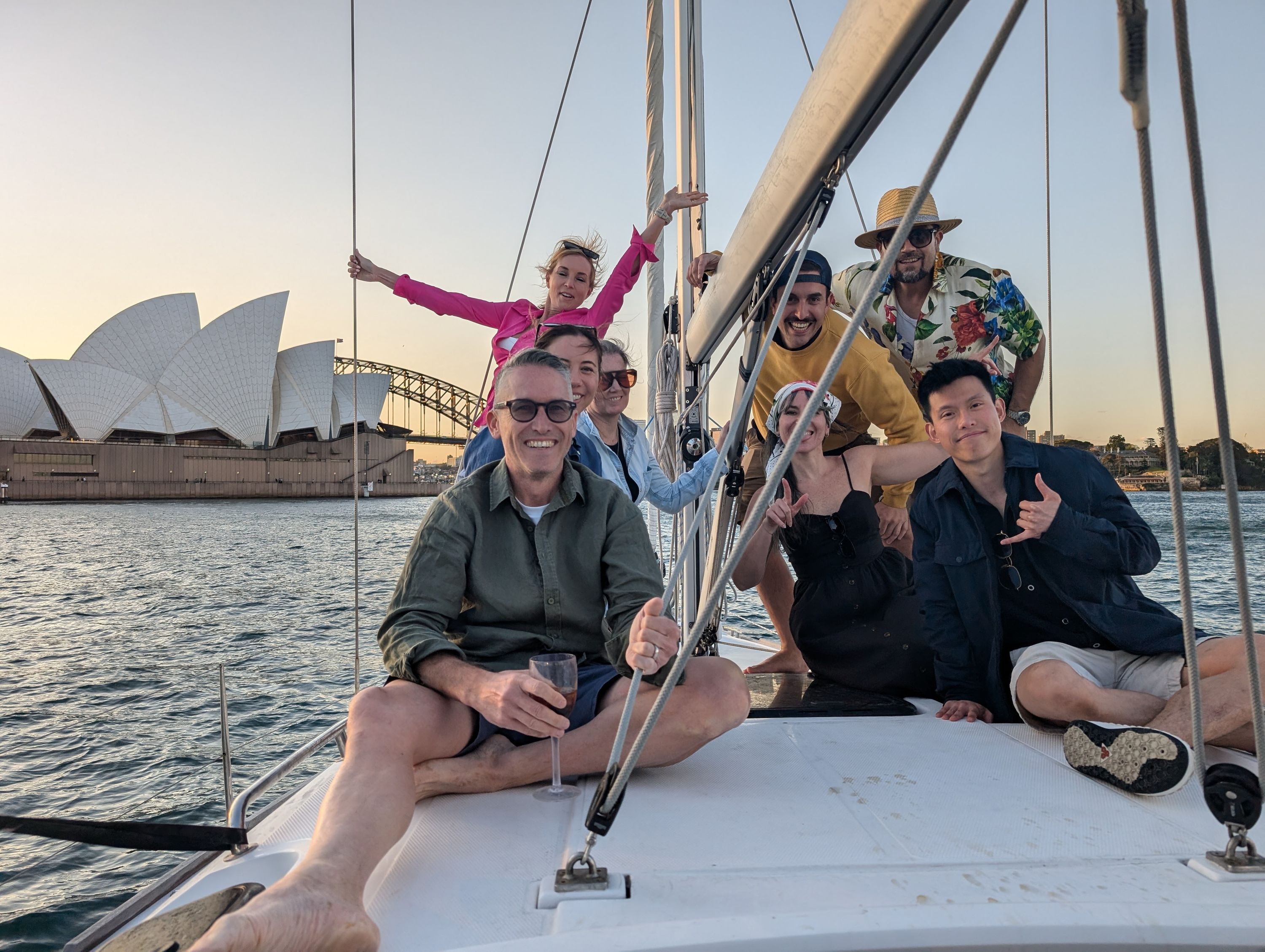 a group of people sitting on the front of a yacht, with the Sydney Opera House in the background