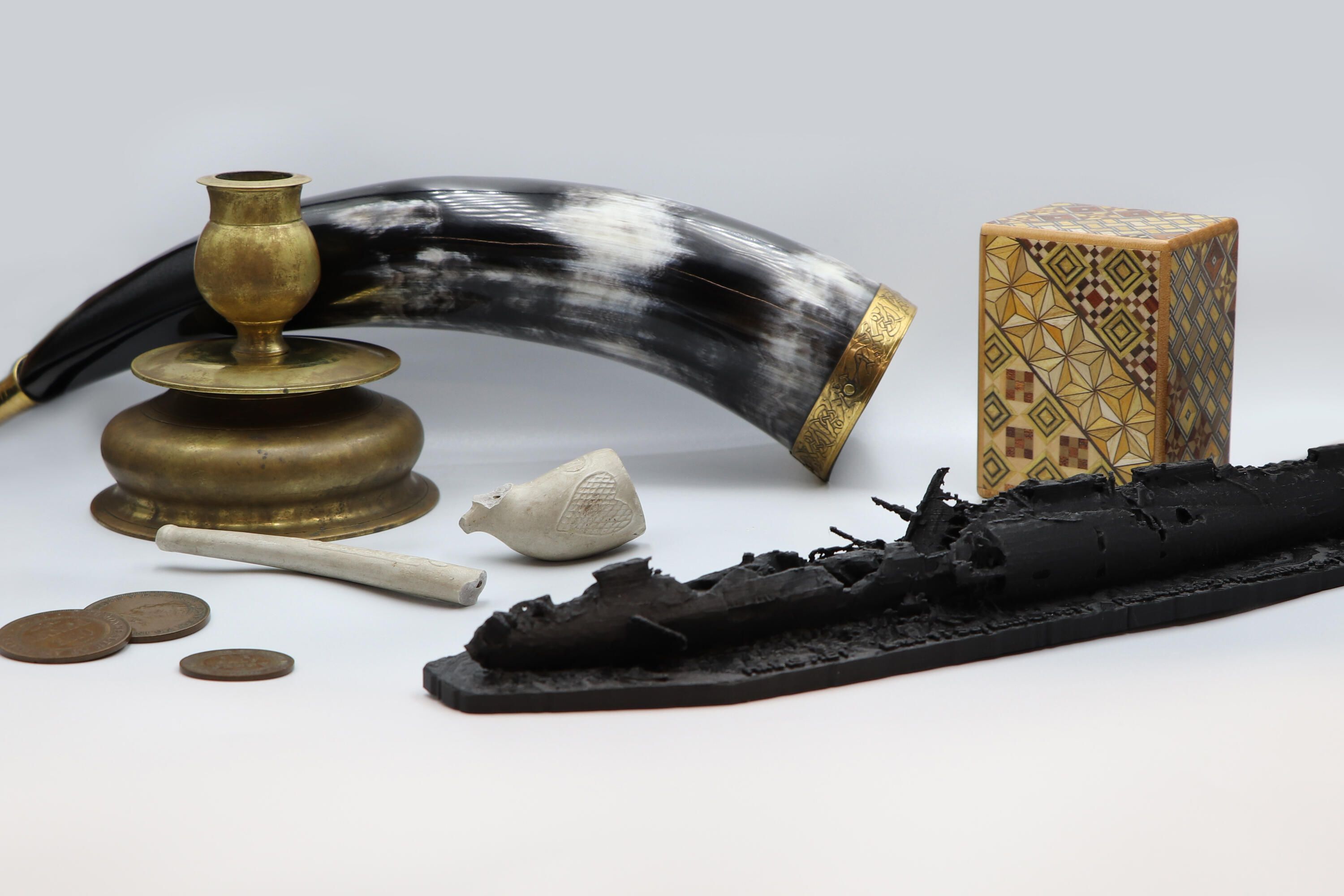 Photo showing a collection of objects including a horn, a candlestick, a broken pipe, coins, a wooden box and a model of a submarine.