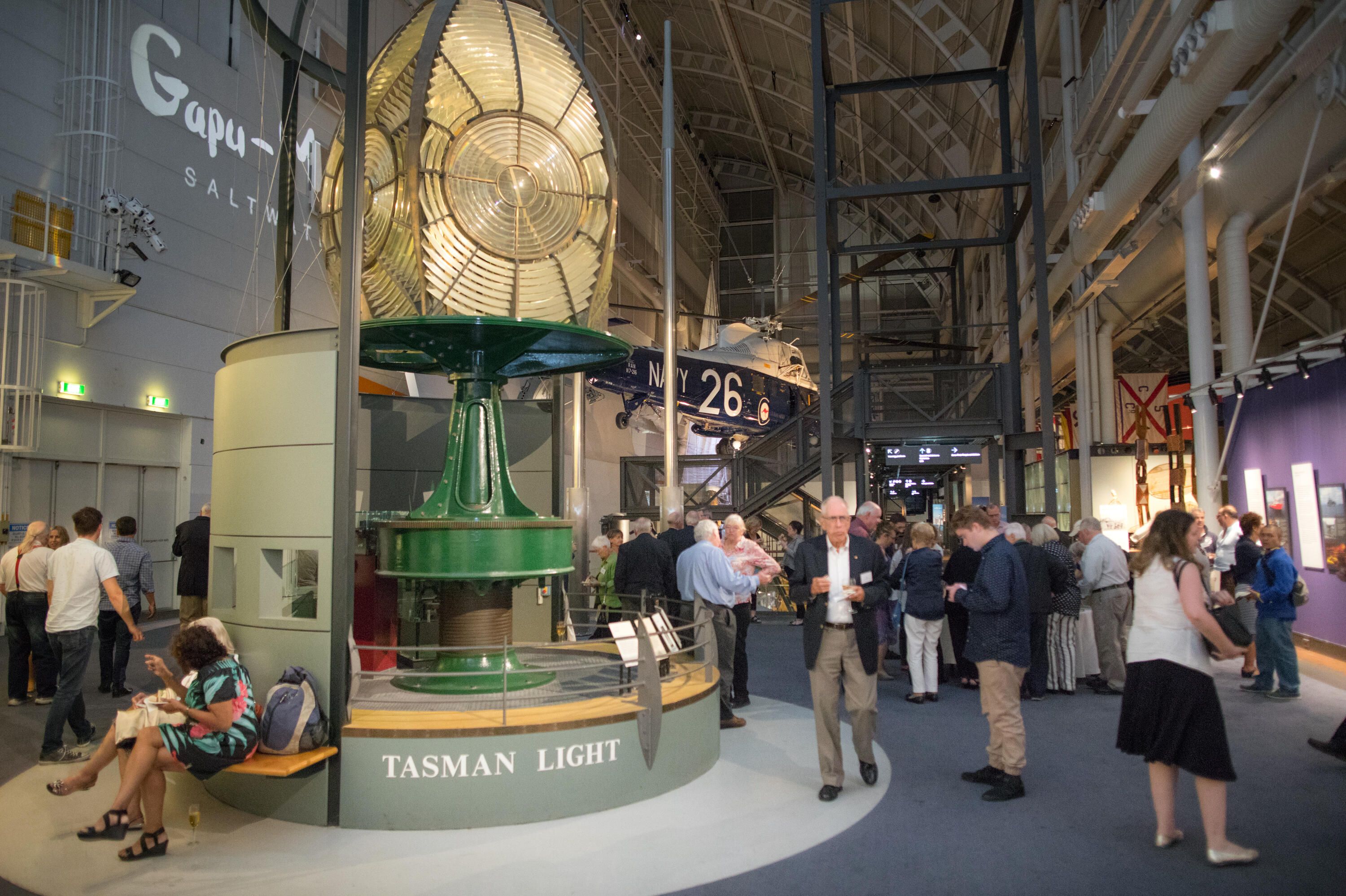 photo of interior space with a lighthouse lens and a crowd of people.