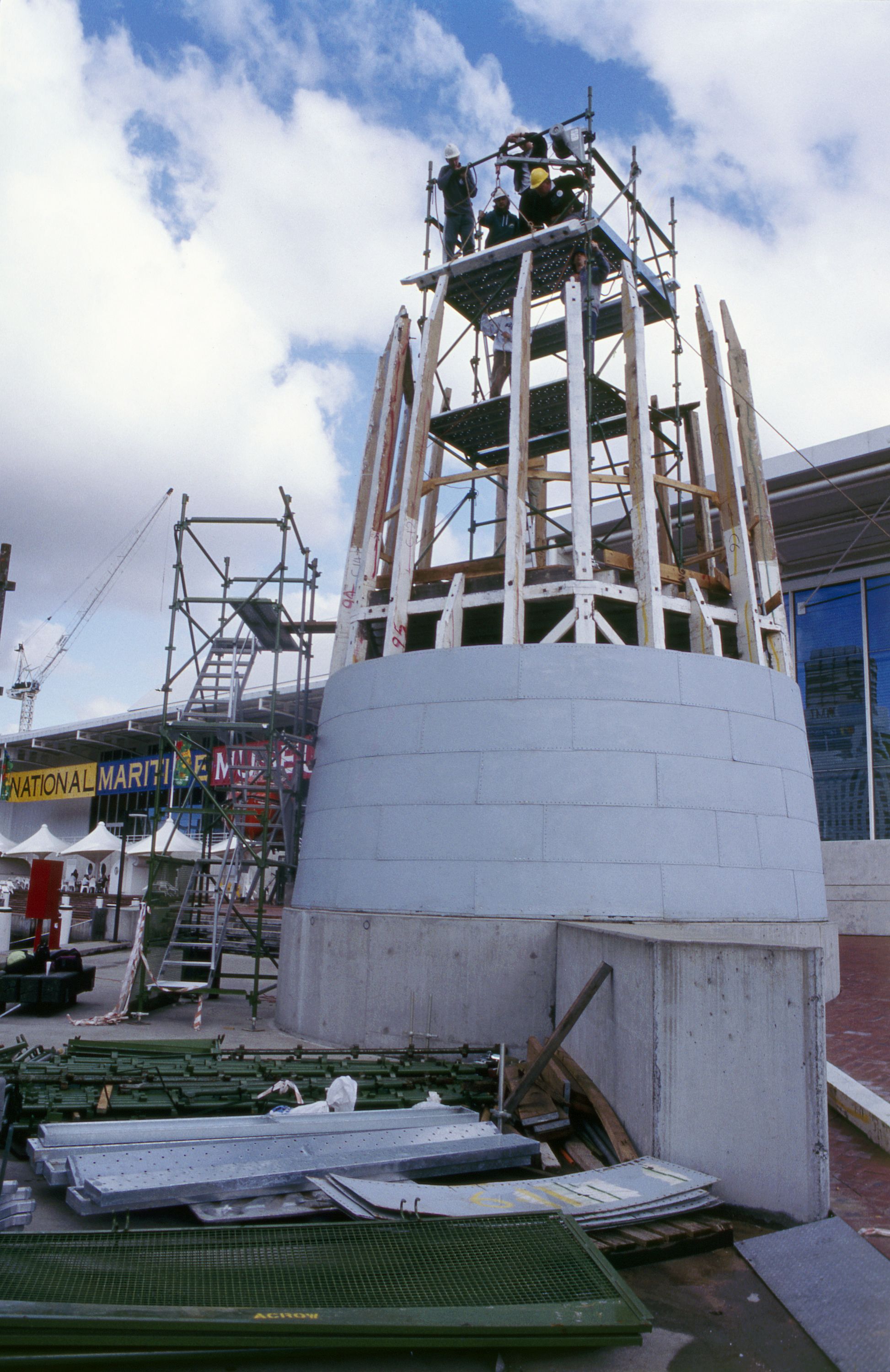 Photo showing the base of a lighthouse being reconstructed, with curved metal panels in the foreground. 